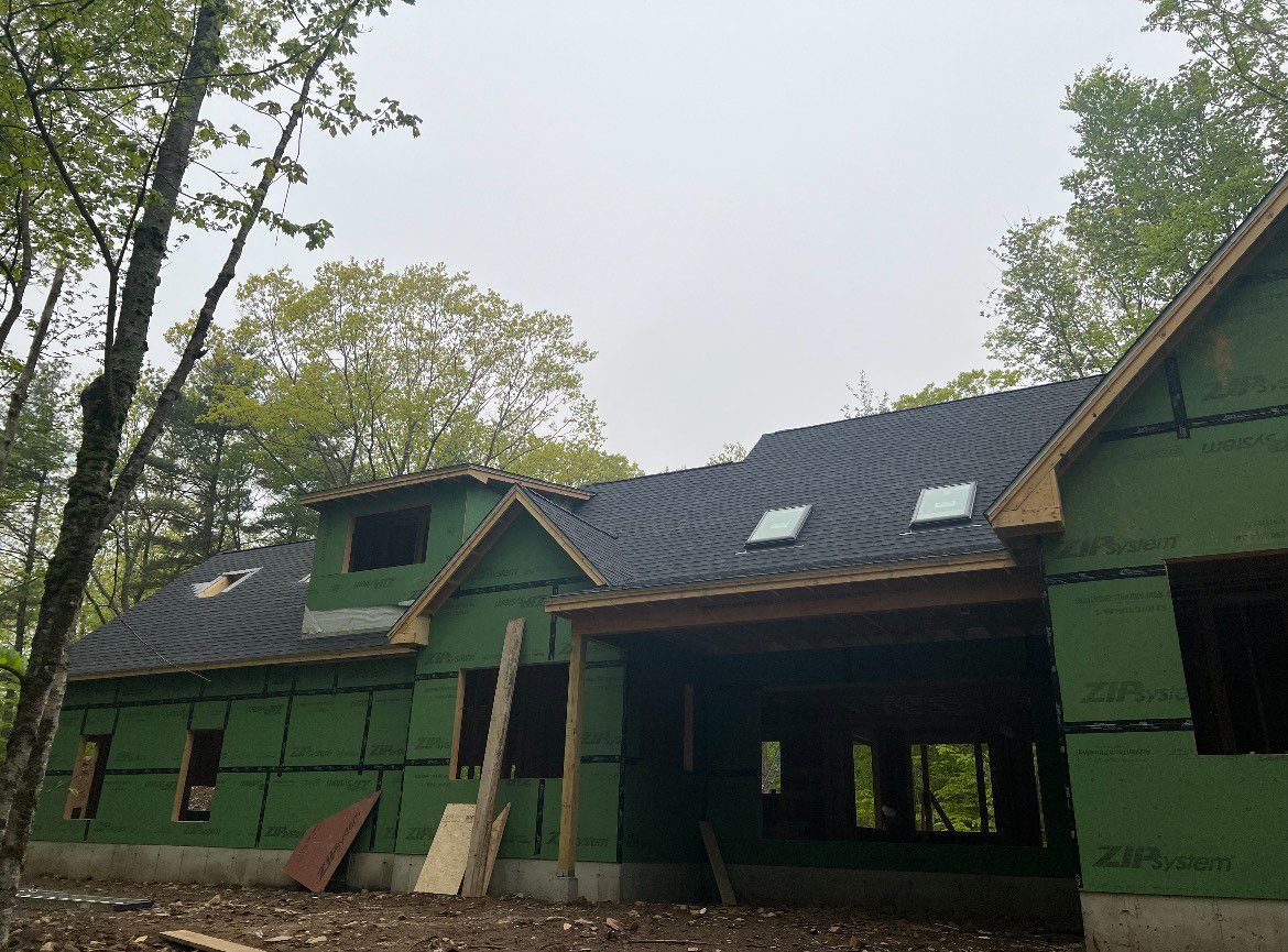 A house is being built in the woods and has a black roof.