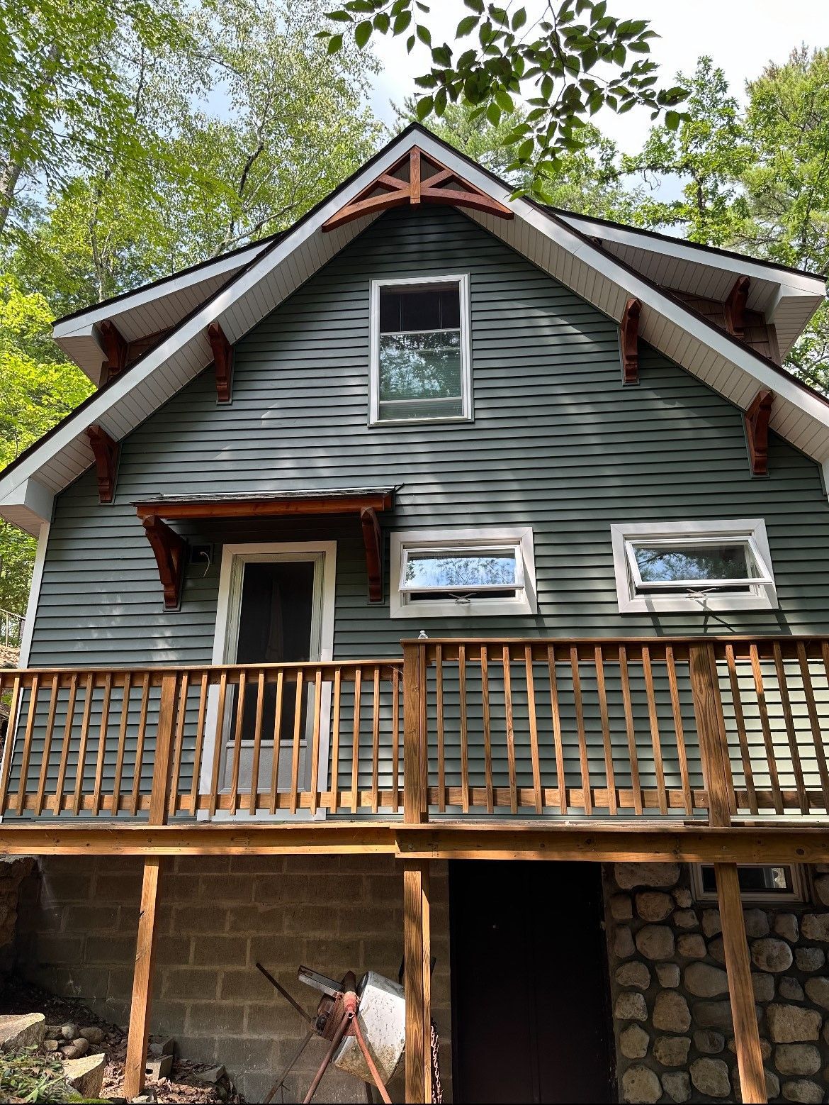 The front of a house with a wooden deck and trees in the background.