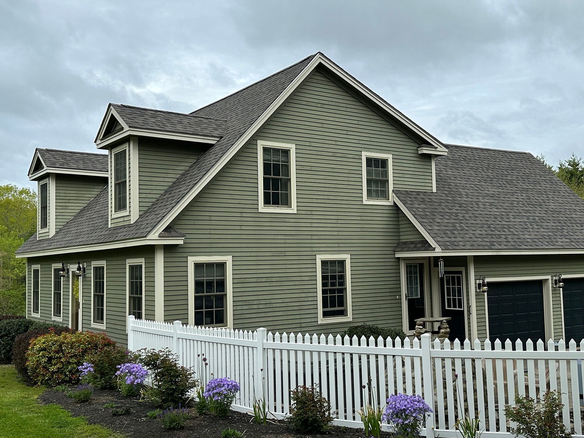 A large green house with a white picket fence in front of it.