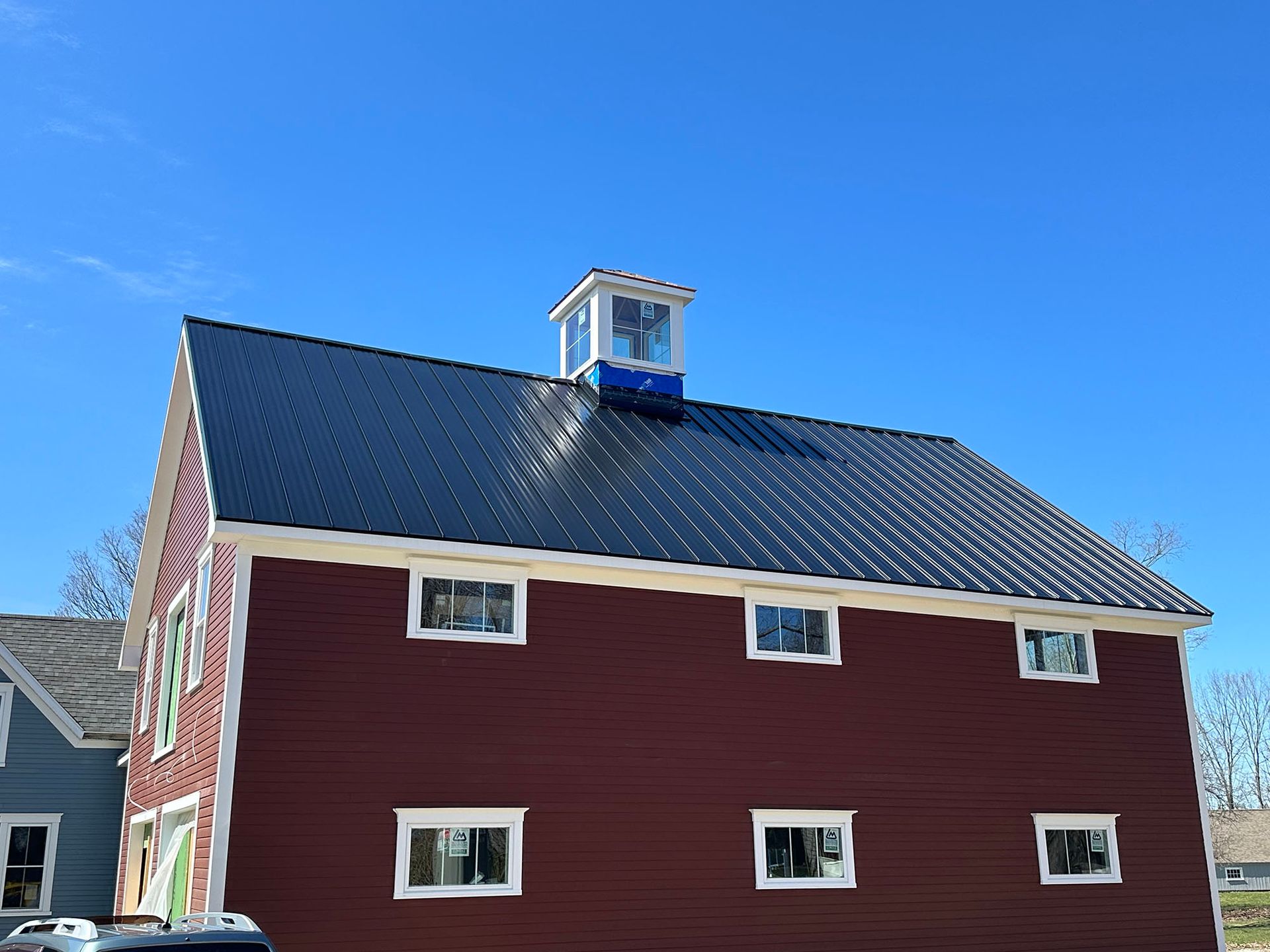 A red barn with a black roof and a cupola on top of it.