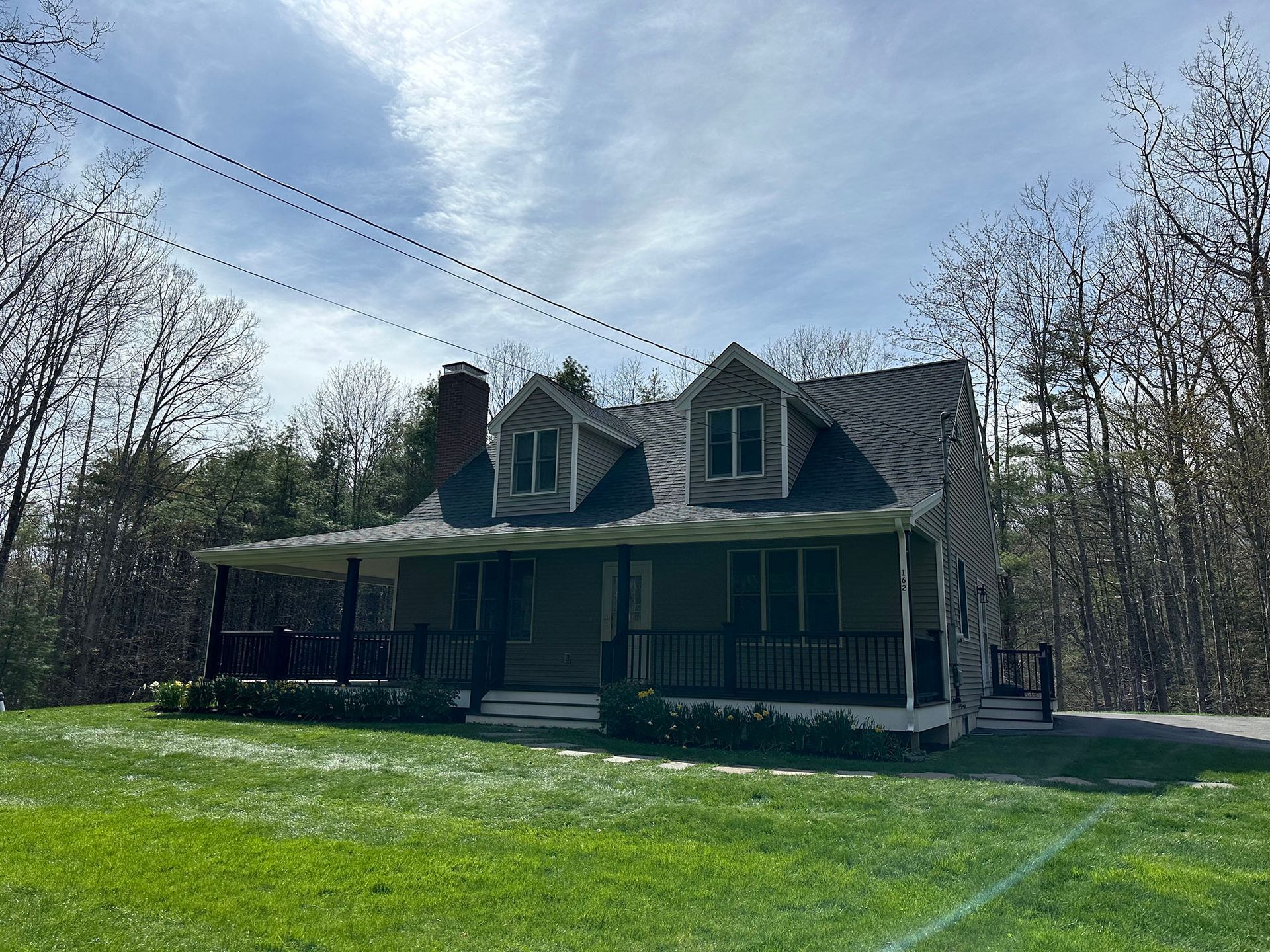 A house with a porch in the middle of a lush green field.