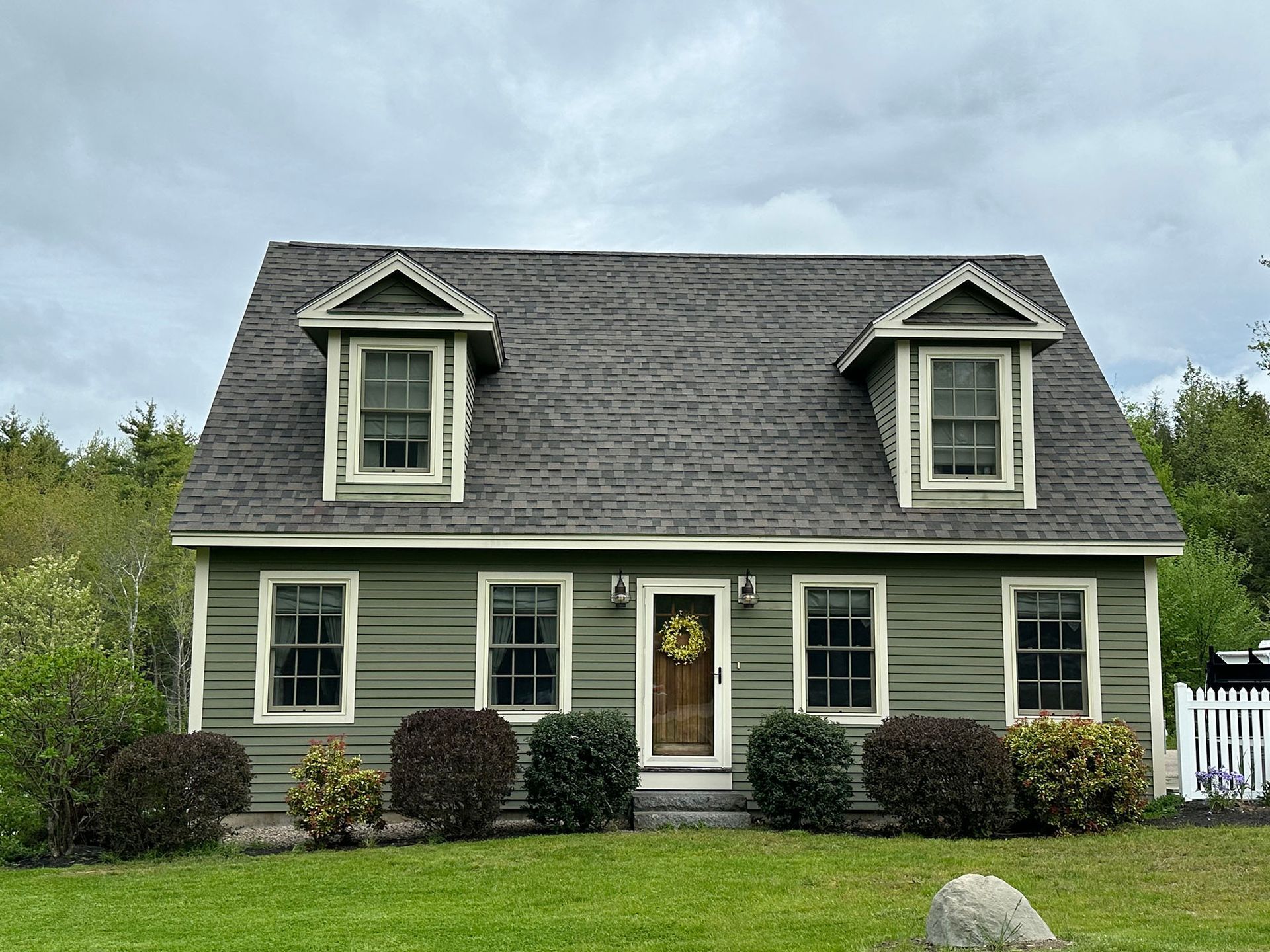 A green house with a gray roof and white trim is sitting on top of a lush green field.