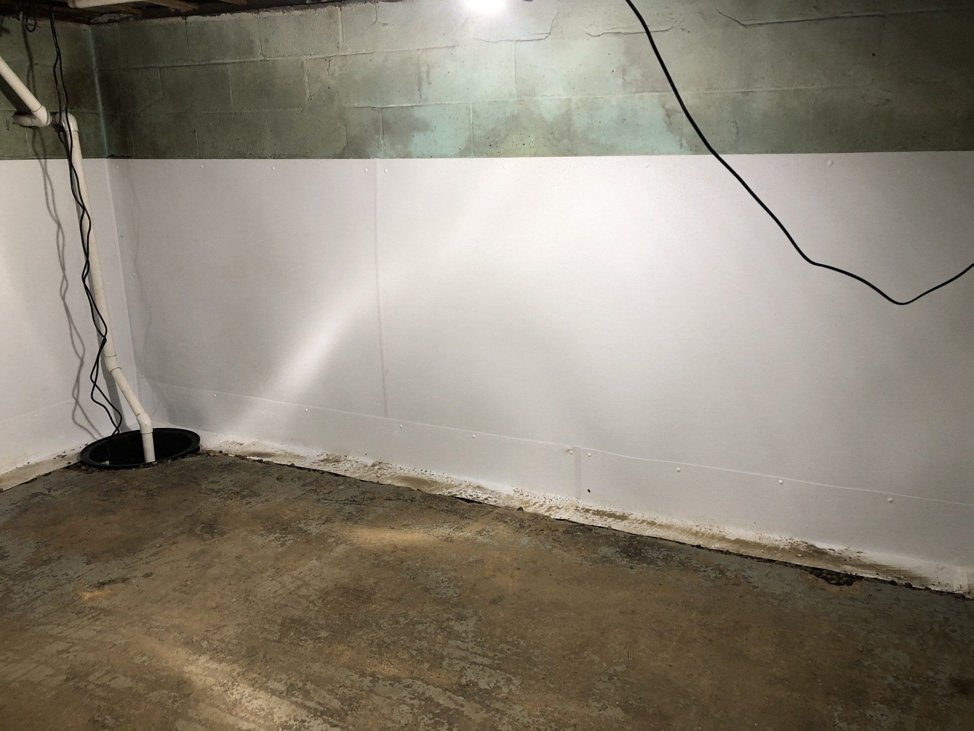 Empty basement with white wall, concrete floor, exposed wiring, and a damp-stained ceiling area