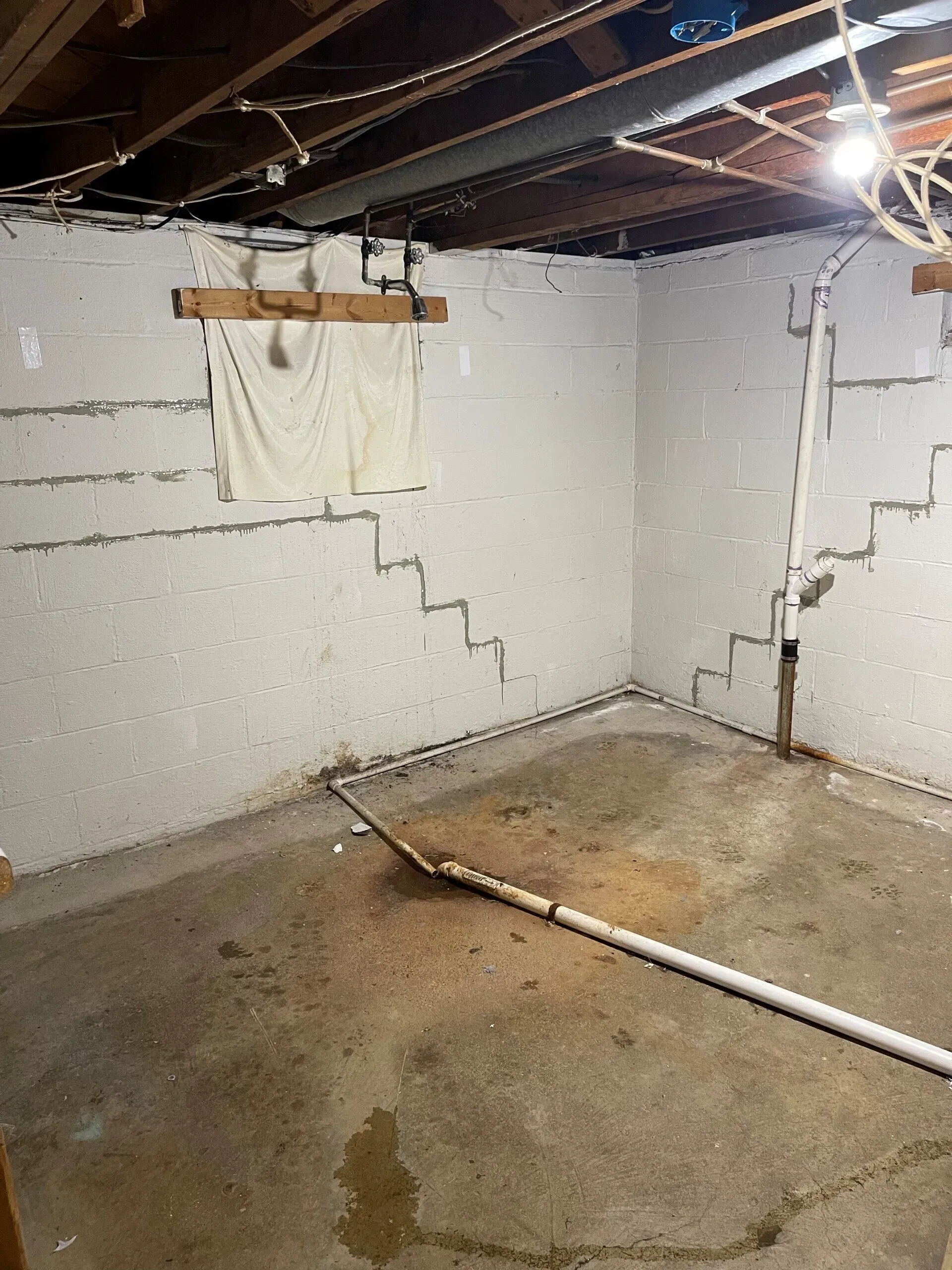 Unfinished basement corner with white cinderblock walls, exposed ceiling beams, and a wet concrete floor.