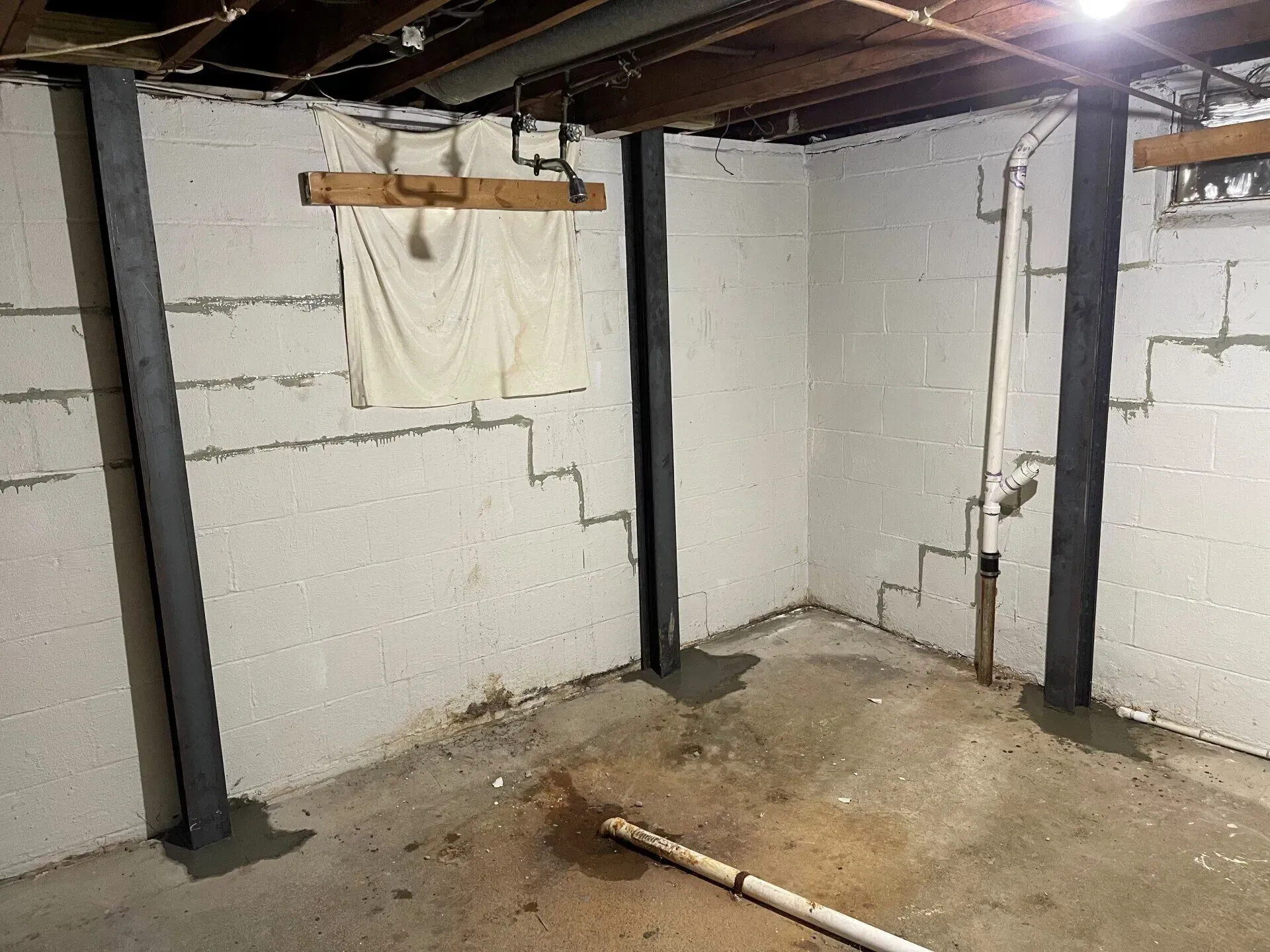 Basement room with white cinderblock walls, exposed ceiling beams, support posts, and a concrete floor.