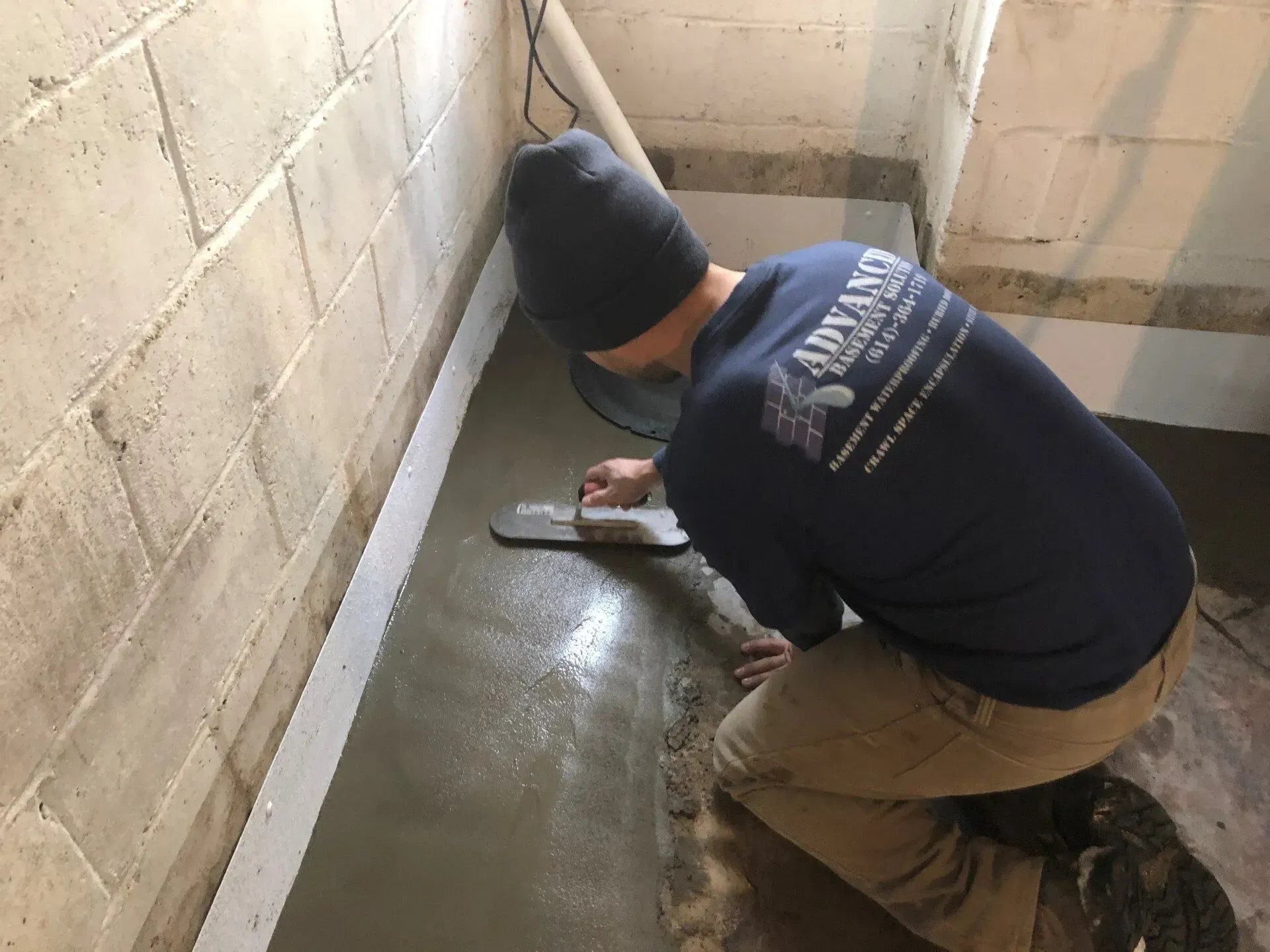 Worker smoothing fresh concrete along a narrow wall in a basement or crawlspace