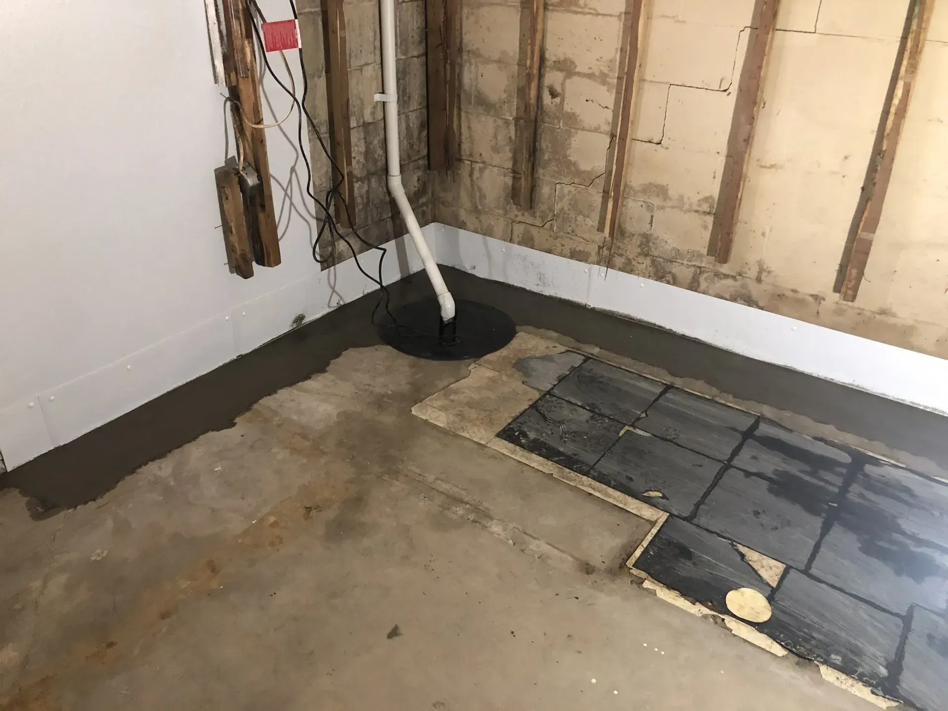 Unfinished basement corner with exposed insulation, floor drain, and concrete floor with a black plastic sheet.