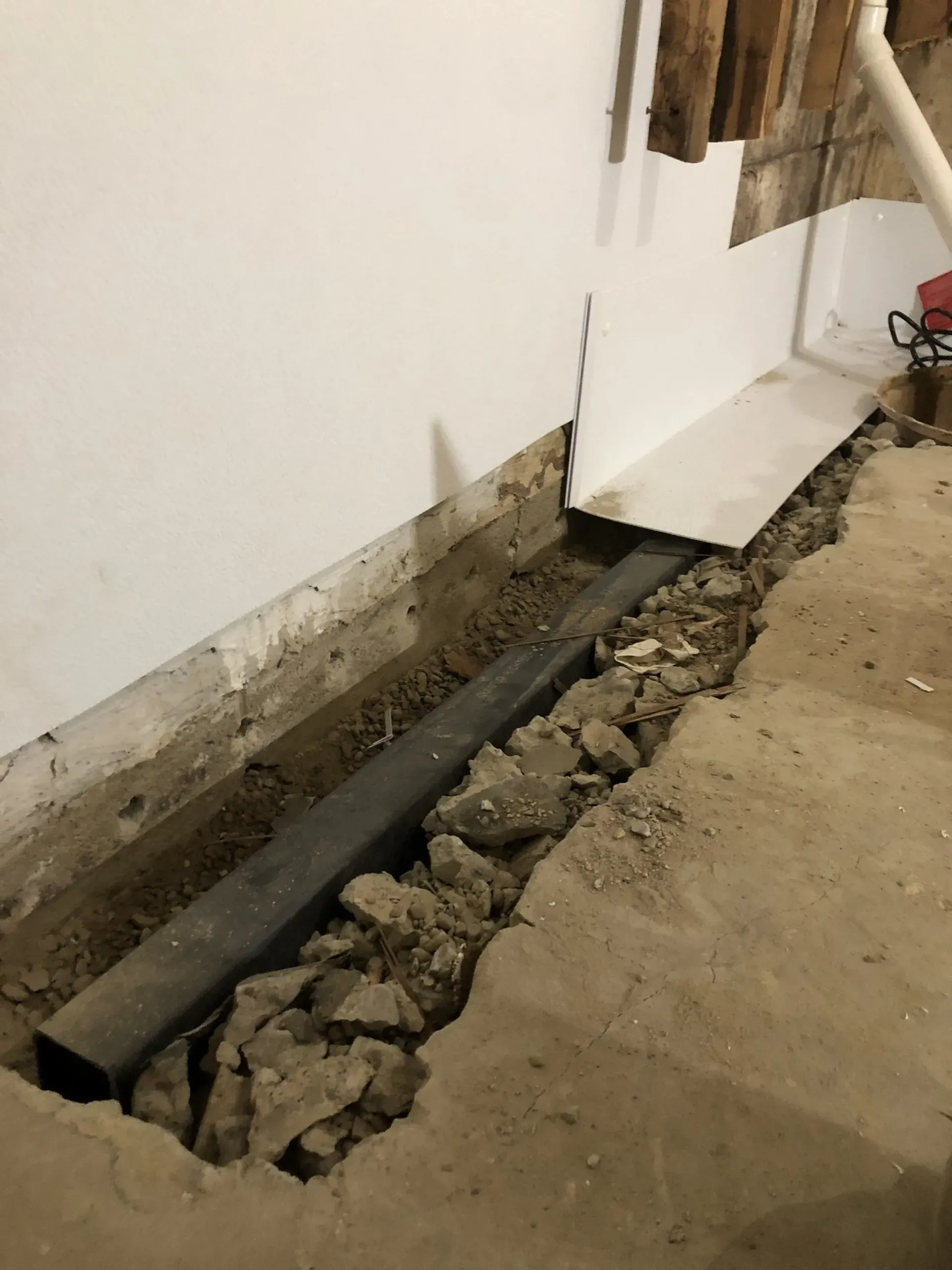 Damaged wall with exposed trench and broken concrete floor inside a building