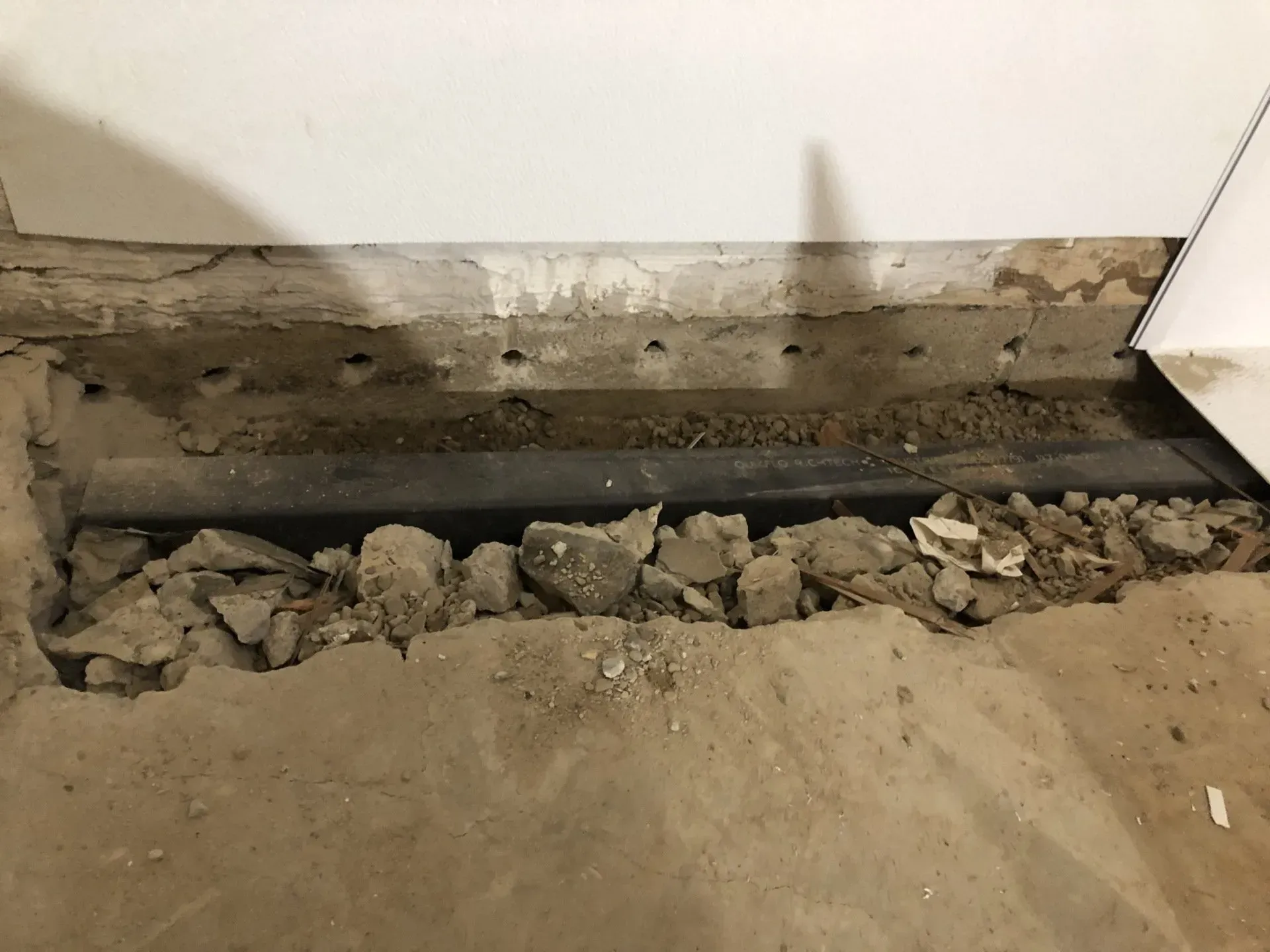 Damaged wall with exposed foundation and rubble on the floor