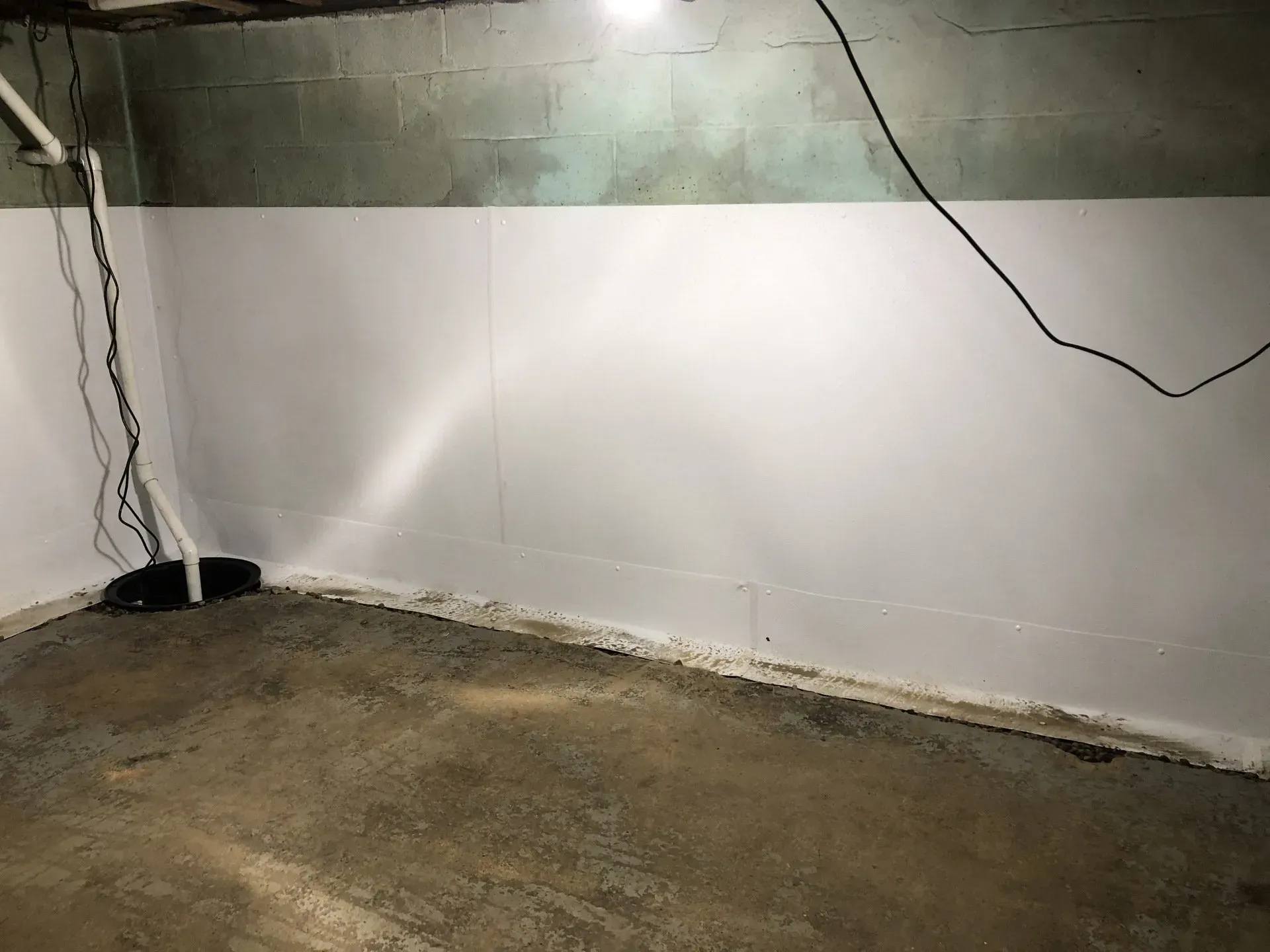 Basement wall with white paneling, exposed concrete above, and loose electrical wires on the floor