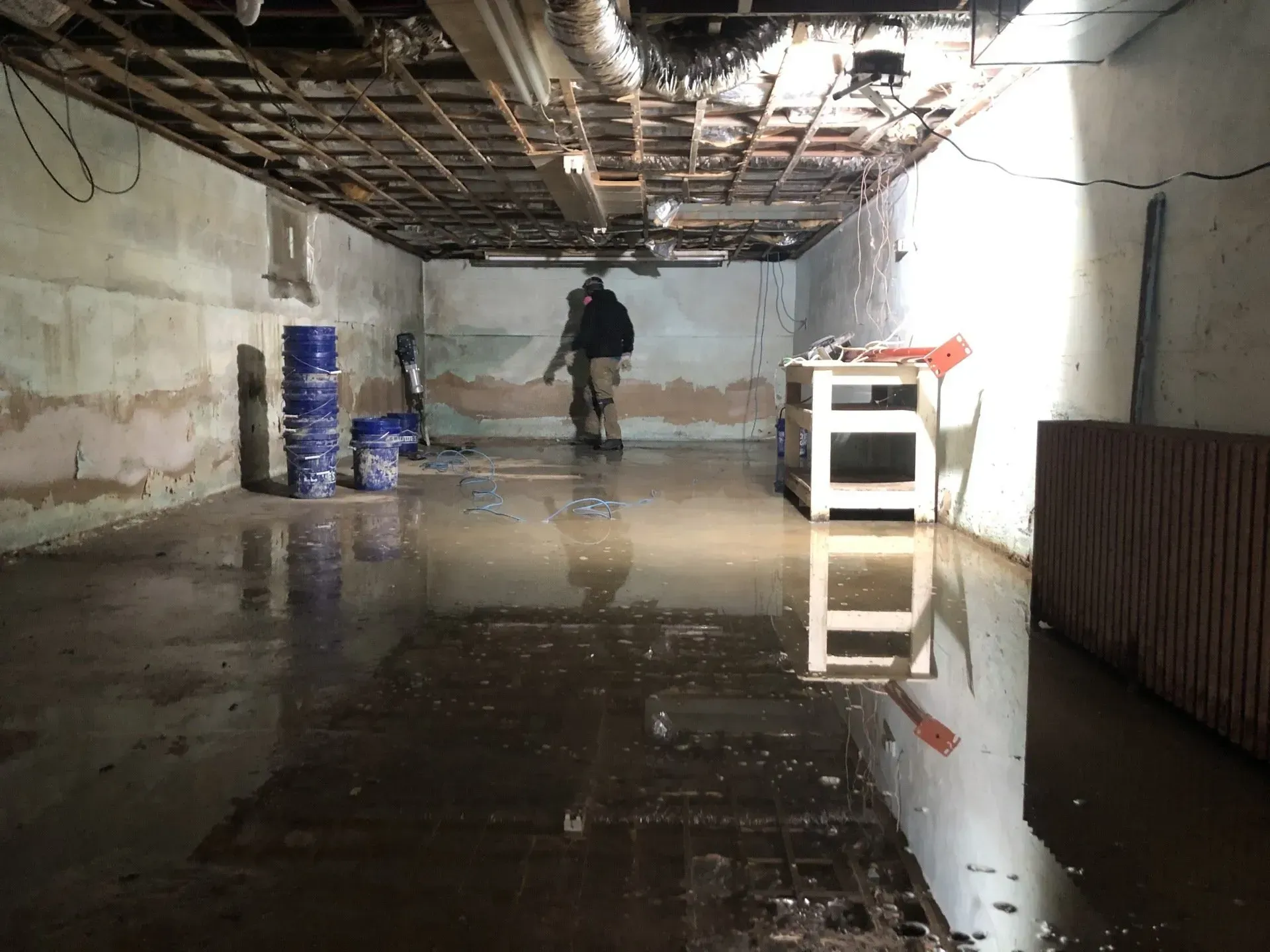 Flooded basement with a worker standing in standing water beneath a damaged ceiling