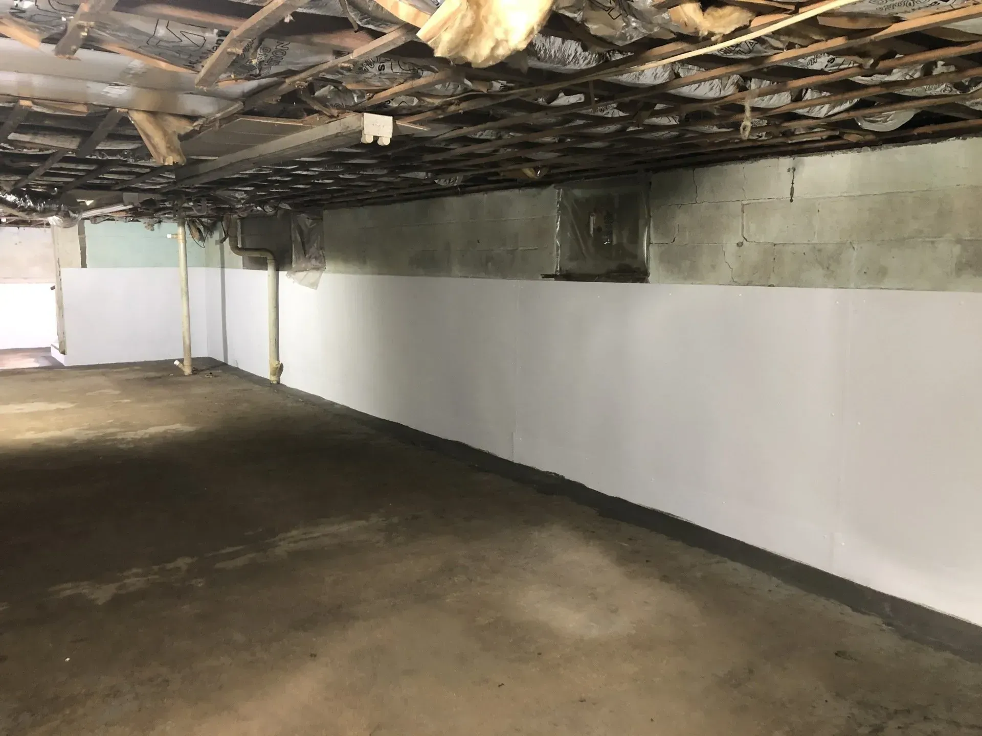 Empty basement with white walls, concrete floor, and exposed ceiling beams