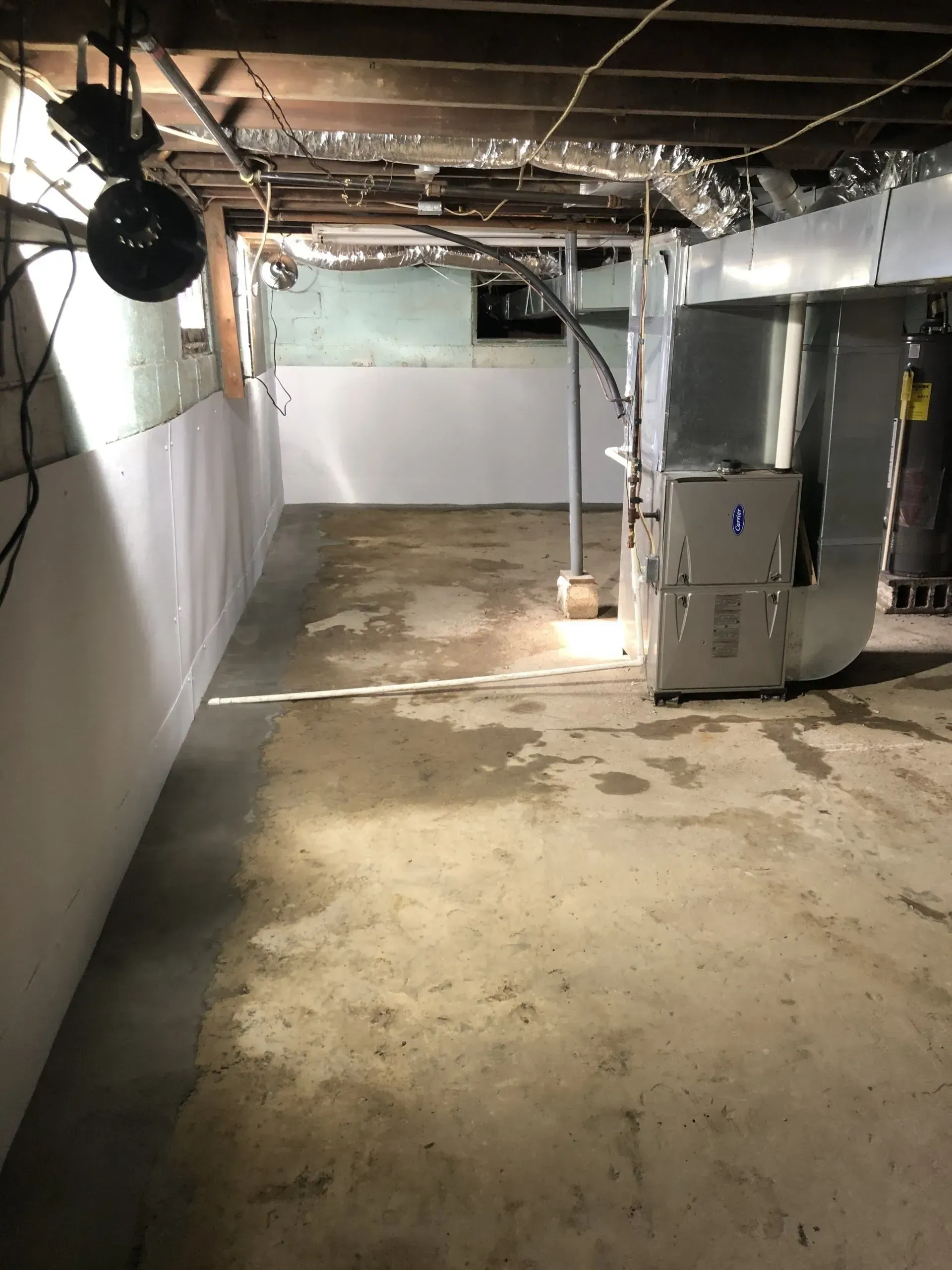 Empty unfinished basement with concrete floor, exposed ceiling pipes, white walls, and a furnace unit.