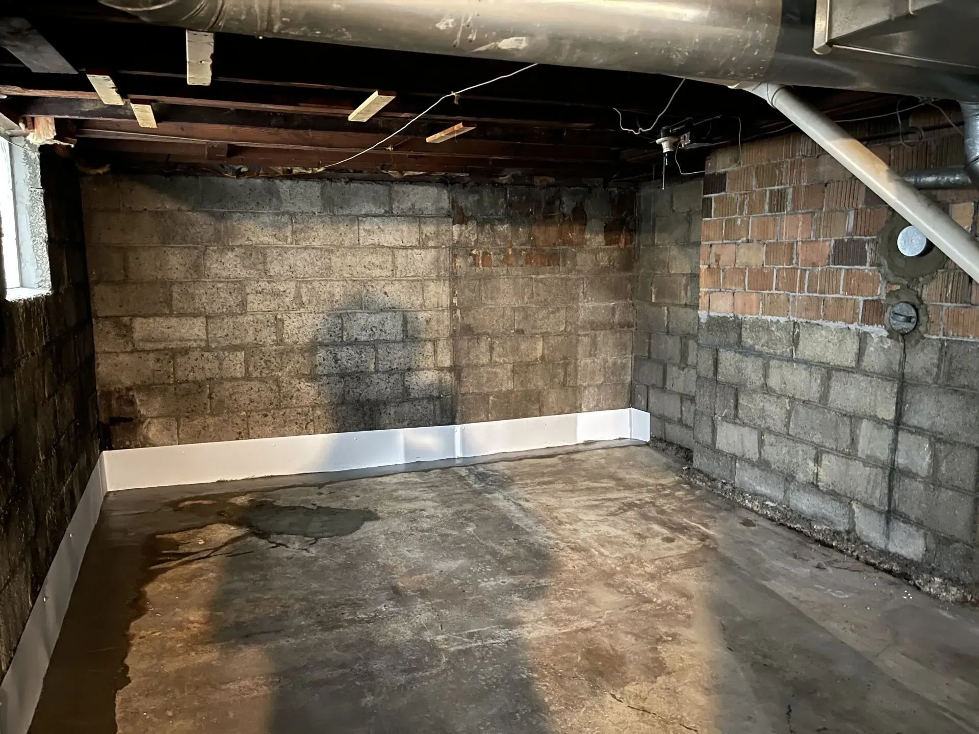 Dim unfinished basement with cinder block walls, exposed beams, and a stained concrete floor.
