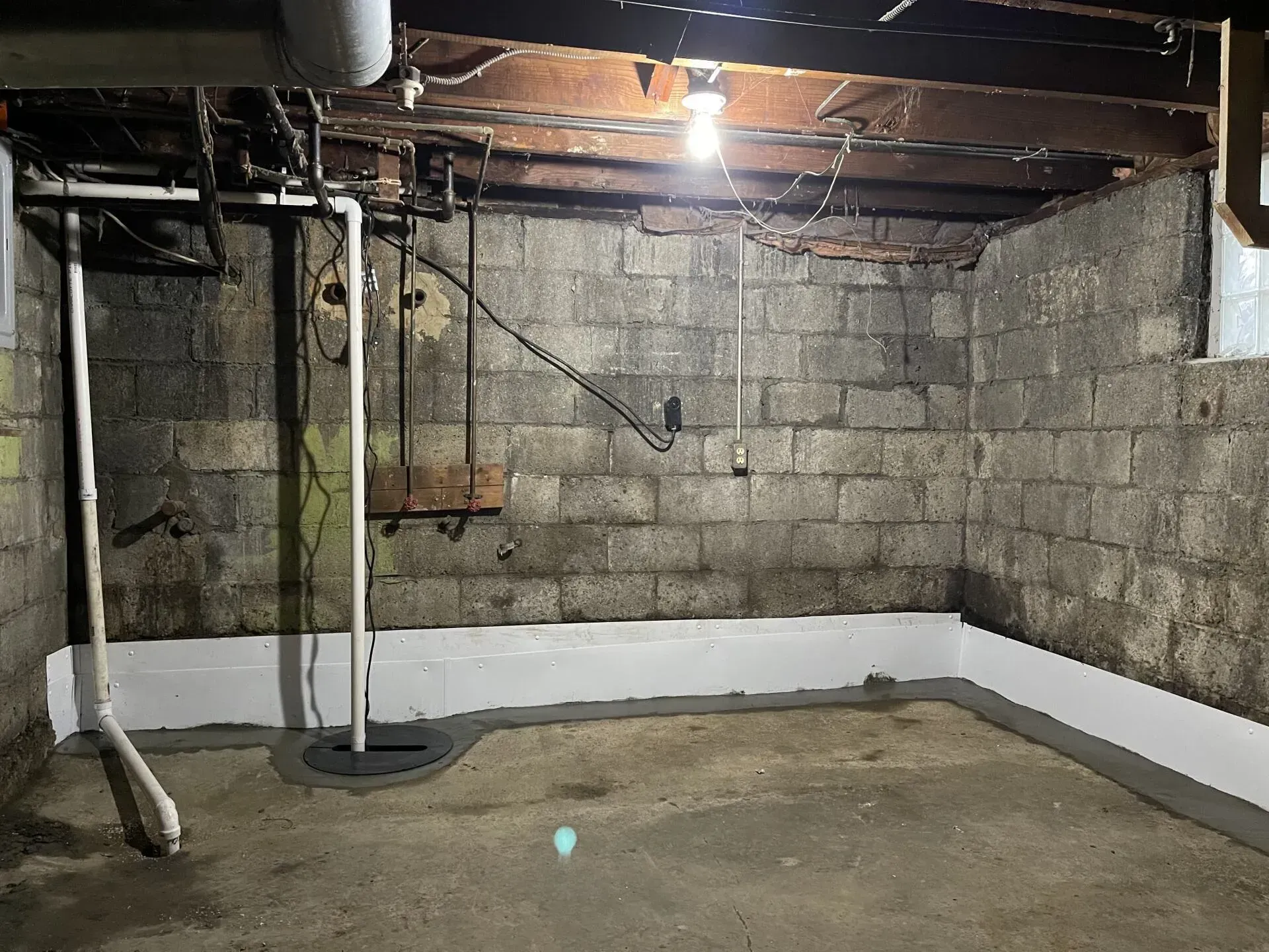 Dim basement with cinderblock walls, exposed pipes, a hanging light, and a bare concrete floor.