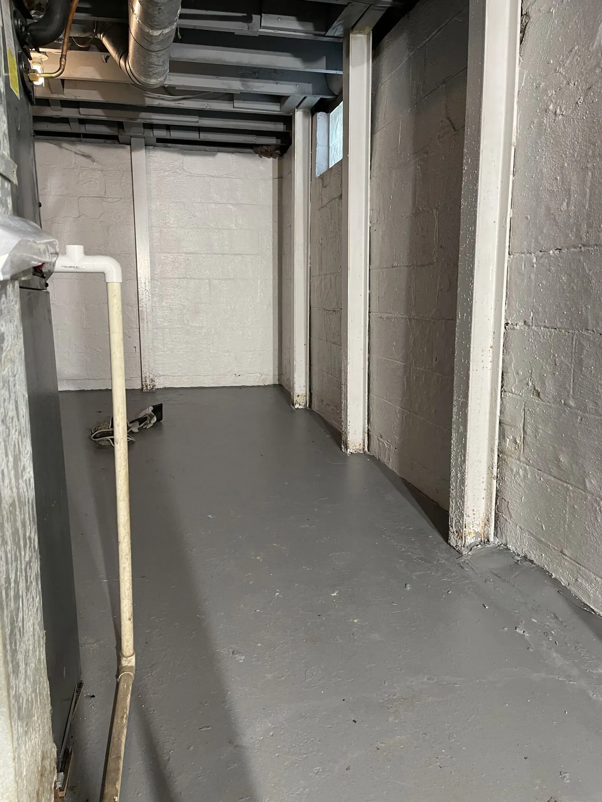 Empty unfinished basement corridor with gray floor, exposed ceiling beams, and cinder block walls