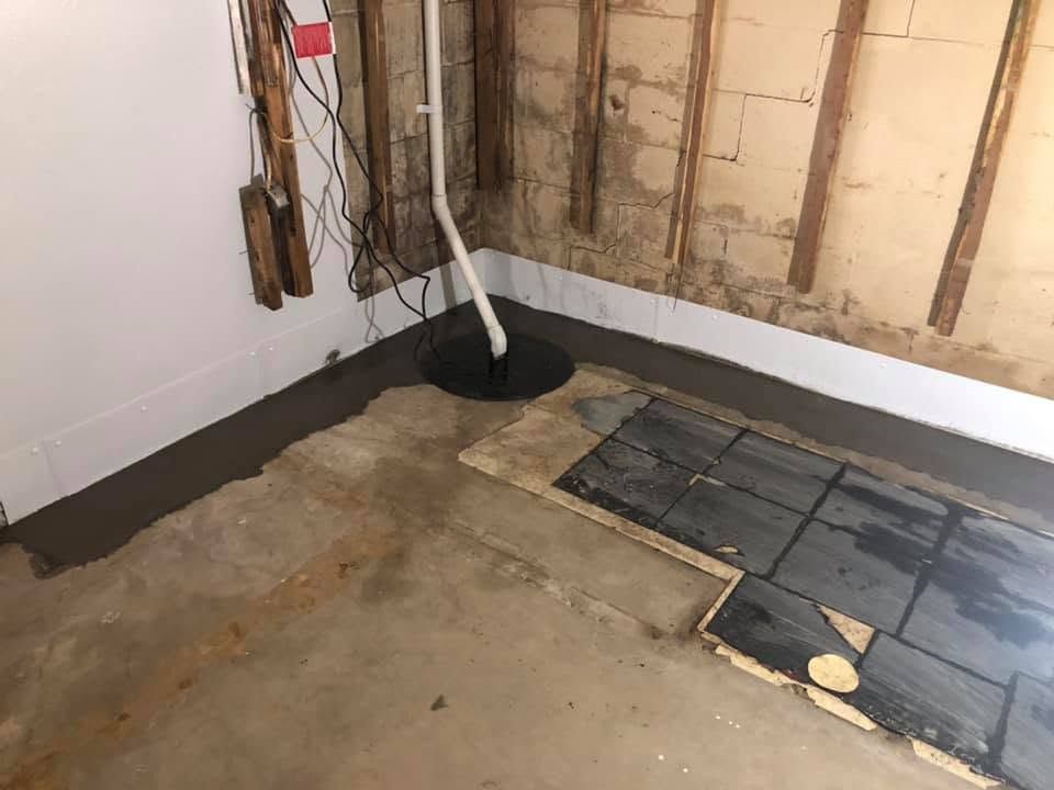 Unfinished basement corner with exposed wall studs, concrete floor, and black plastic sheeting.