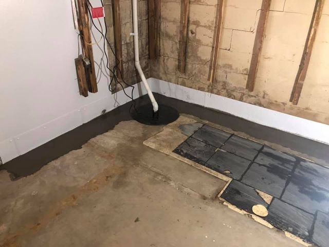 Unfinished basement corner with exposed wall studs, concrete floor, and black plastic sheeting.