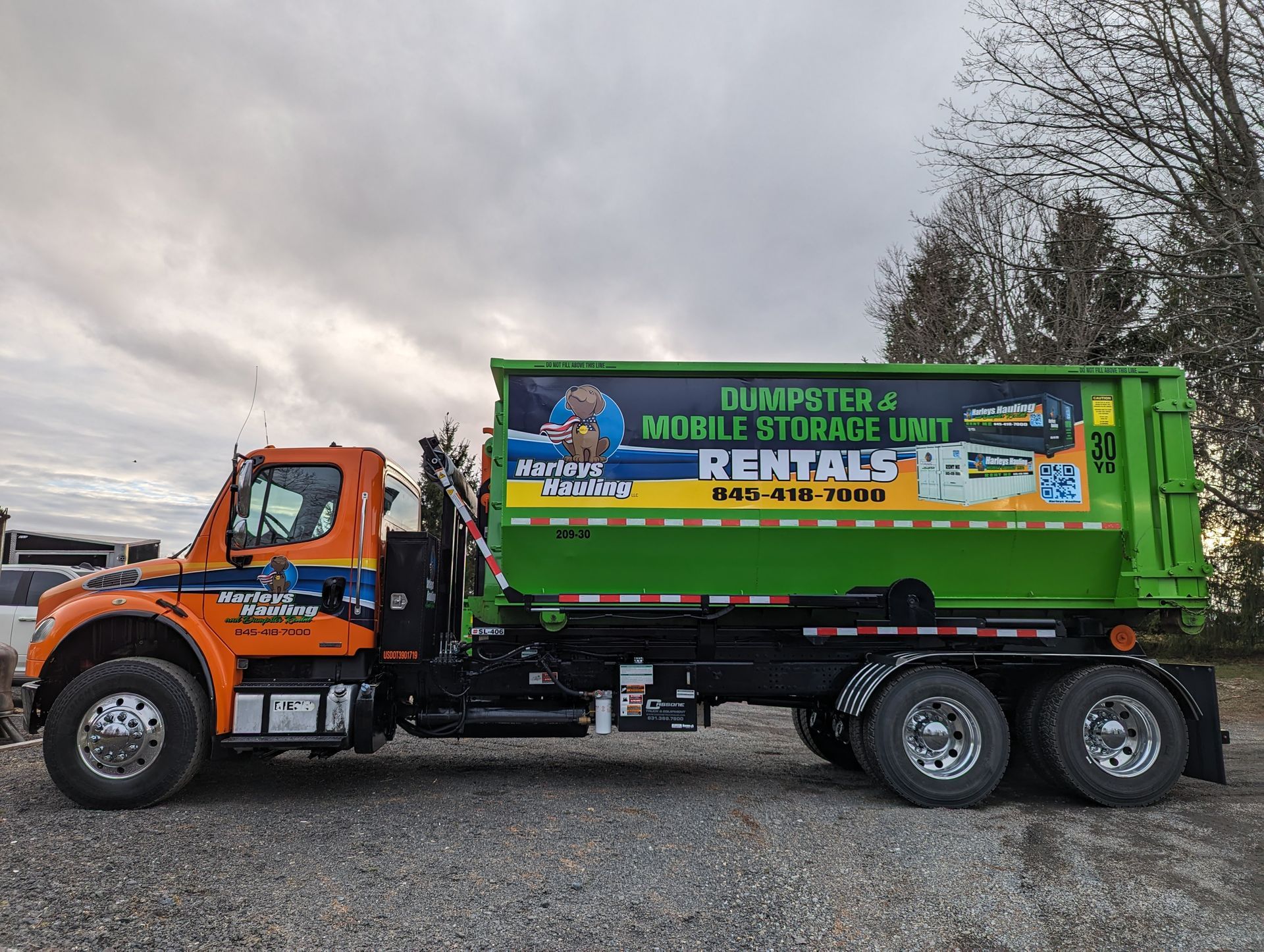 Orange and green rental dump truck parked outdoors under a cloudy sky