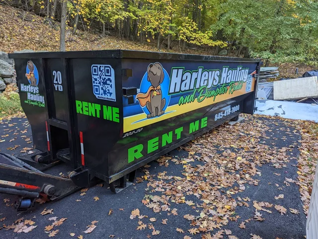 Harley’s Hauling dumpster trailer with bright green “RENT ME” signs on a leaf-covered road