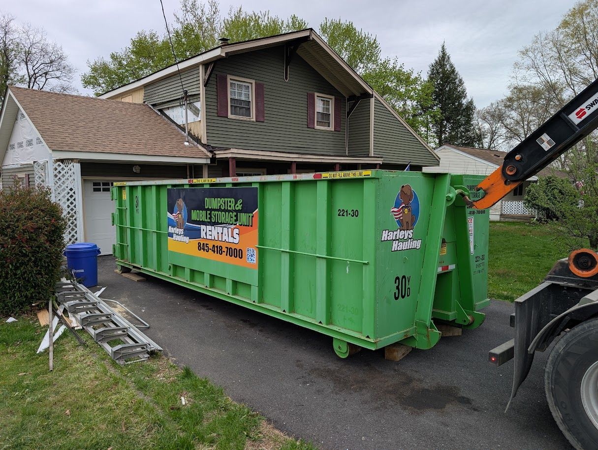 Green construction dumpster beside a house with a front loader nearby on a driveway