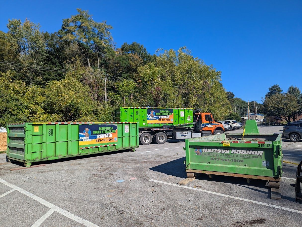 Green dumpsters and trucks in a gravel lot with trees in the background