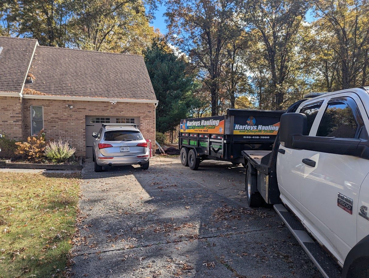 White pickup and trailer in a driveway beside a brick house with a silver SUV under the carport.