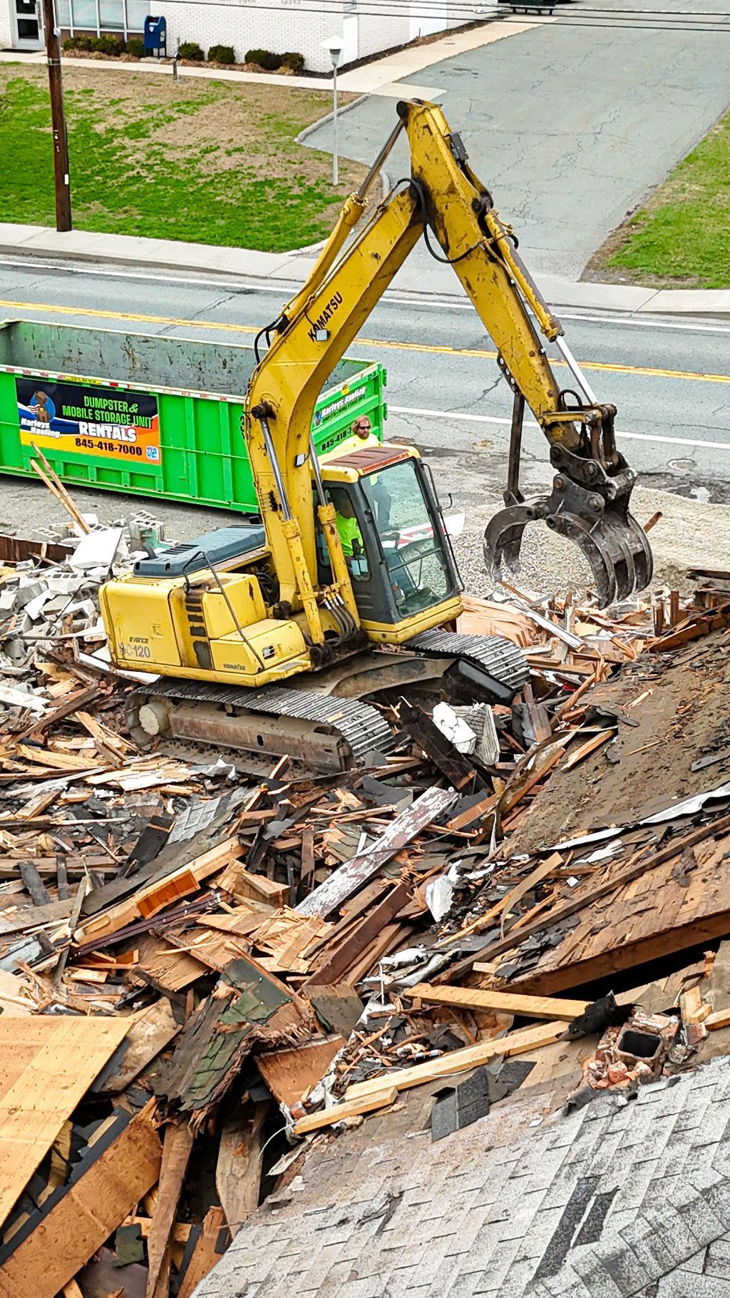 Yellow excavator demolishing debris at a construction site beside a road