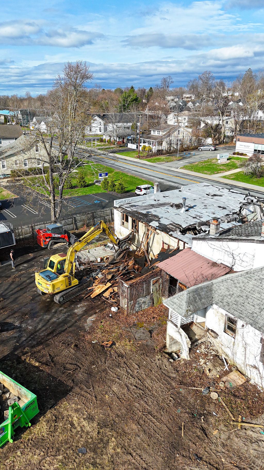 Demolition site with excavator clearing debris beside houses under a blue sky