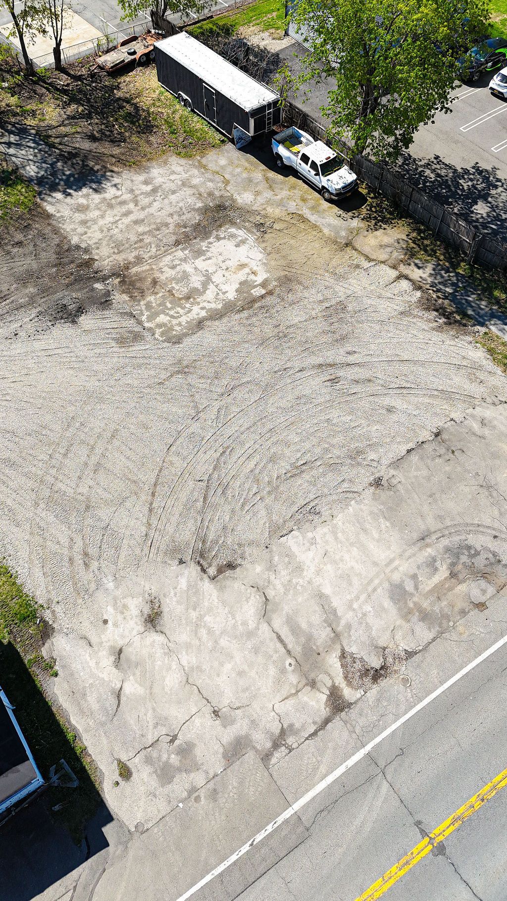 Empty dirt lot beside a road, with a white truck and small structure at the top edge.