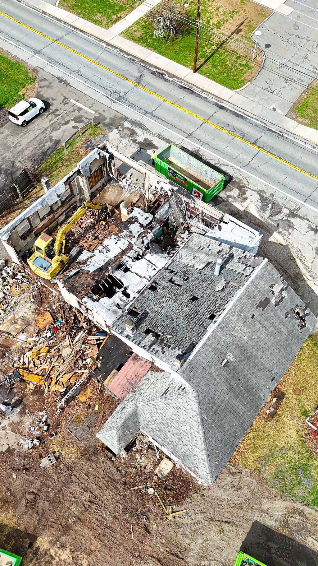Aerial view of a house demolition site with heavy machinery, debris, and a nearby green truck.