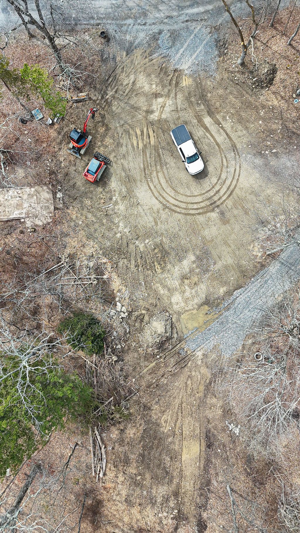 White SUV on dirt clearing with two people and a red ATV nearby in a sparse wooded area