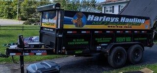 Harleys Hauling dump trailer parked on grass beside a road, with a black truck