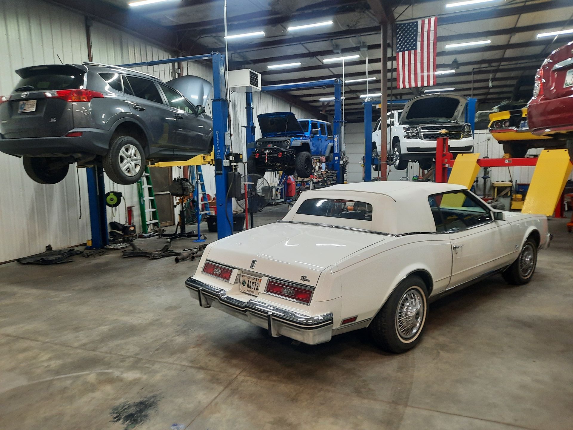 A white car is parked in a garage with other cars.