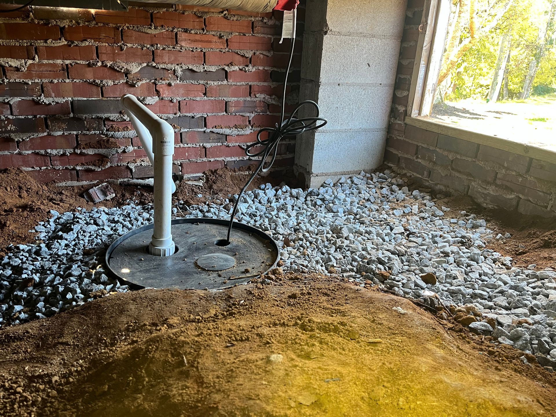 A drain in a basement next to a brick wall and a window.