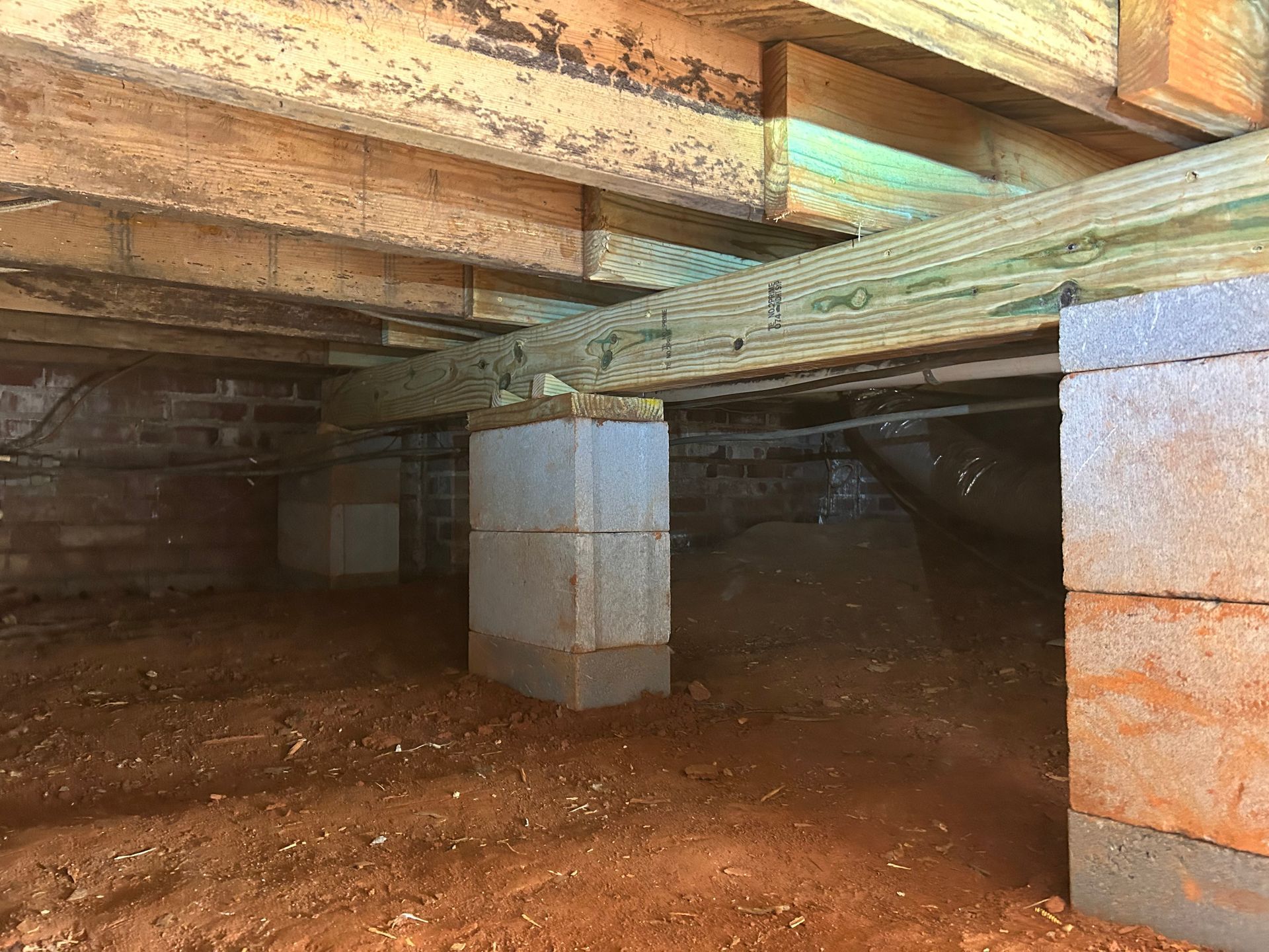 A crawl space under a house with wooden beams and concrete blocks.