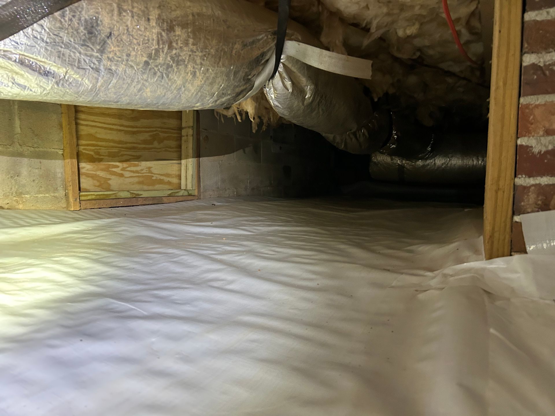 A crawl space with a lot of insulation and a brick wall.