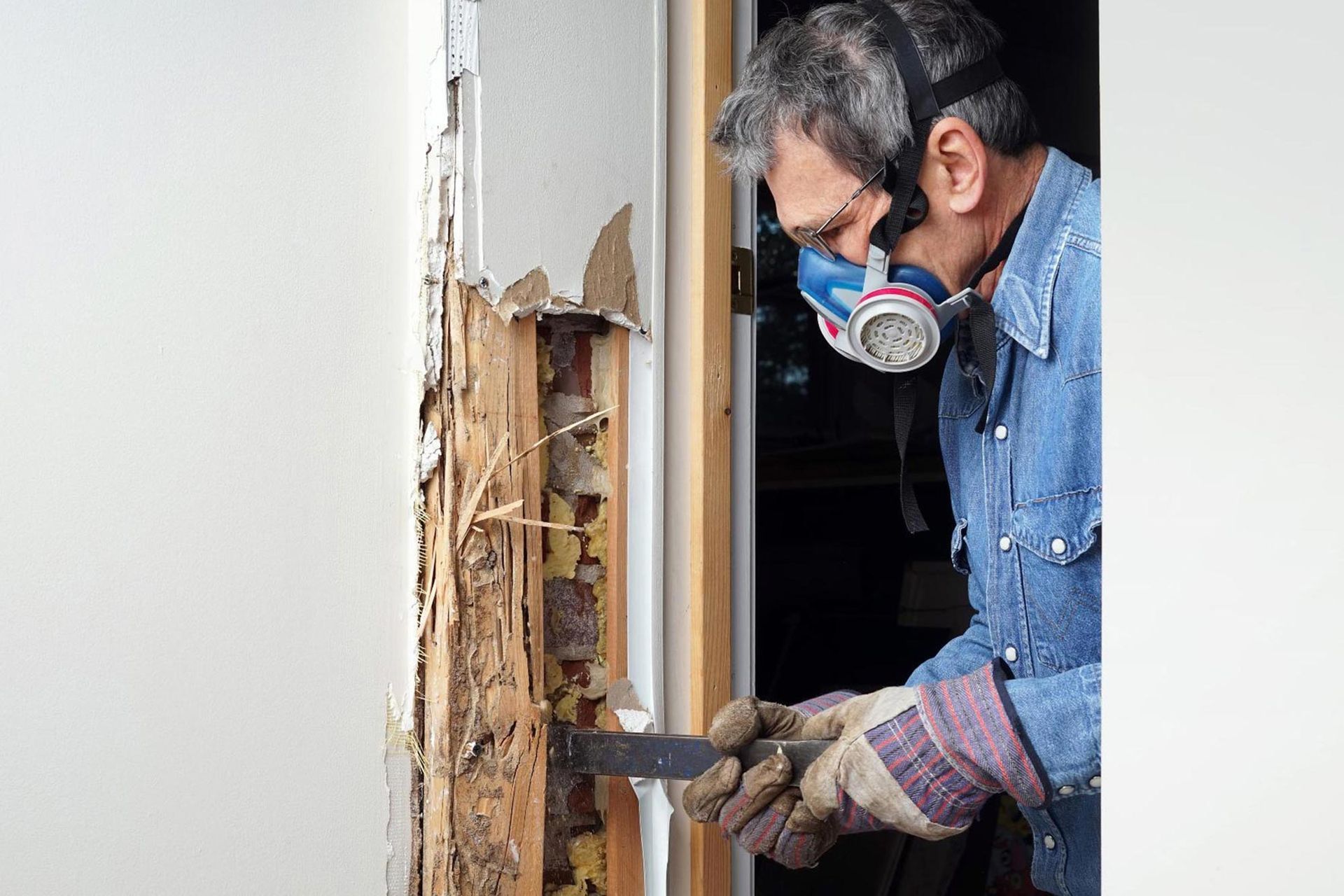 A man wearing a gas mask is working on a termite infested wall.