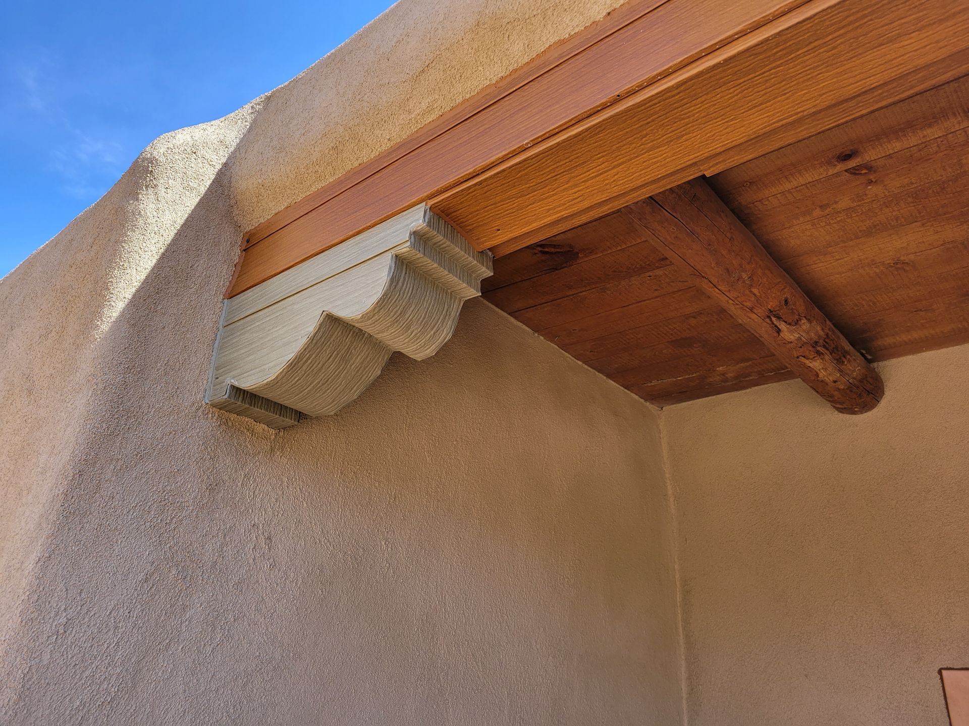 Beige stucco building corner with a wooden beam ceiling and decorative corbel.