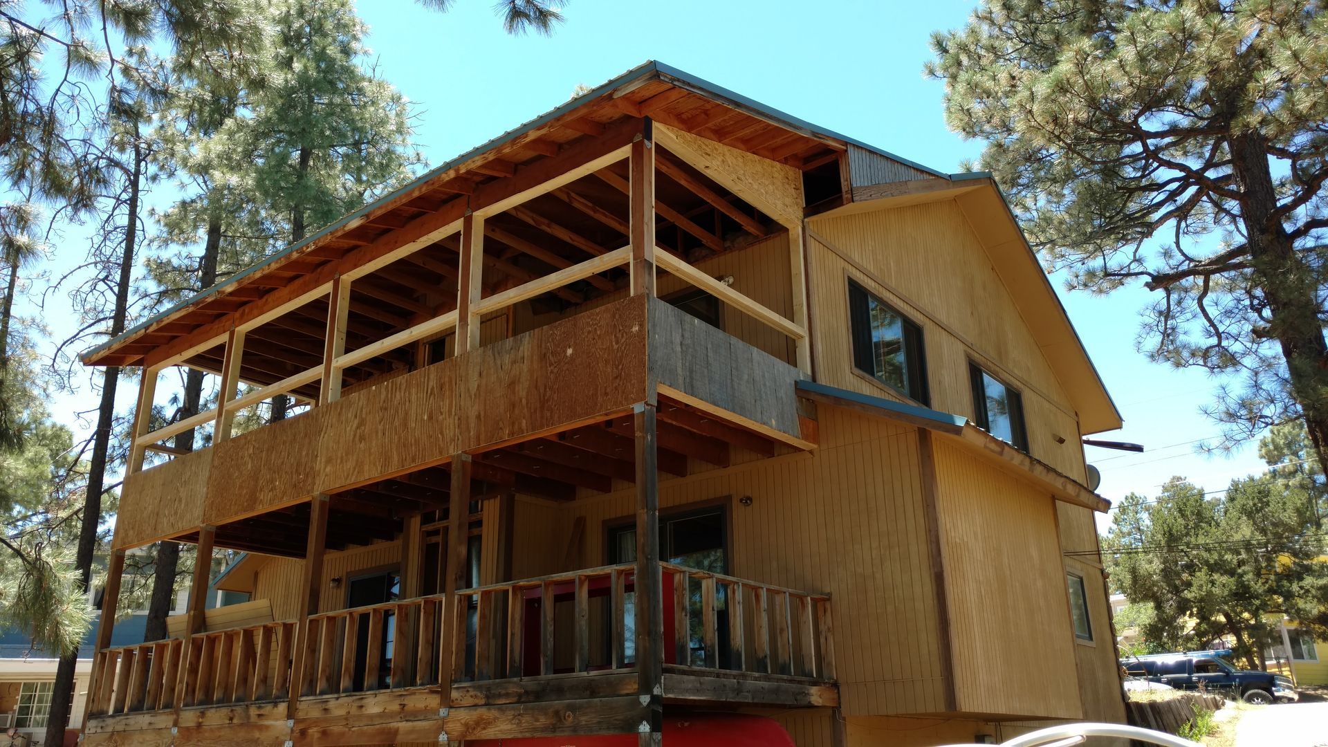 Two-story wooden house with balconies, surrounded by trees, under a blue sky.