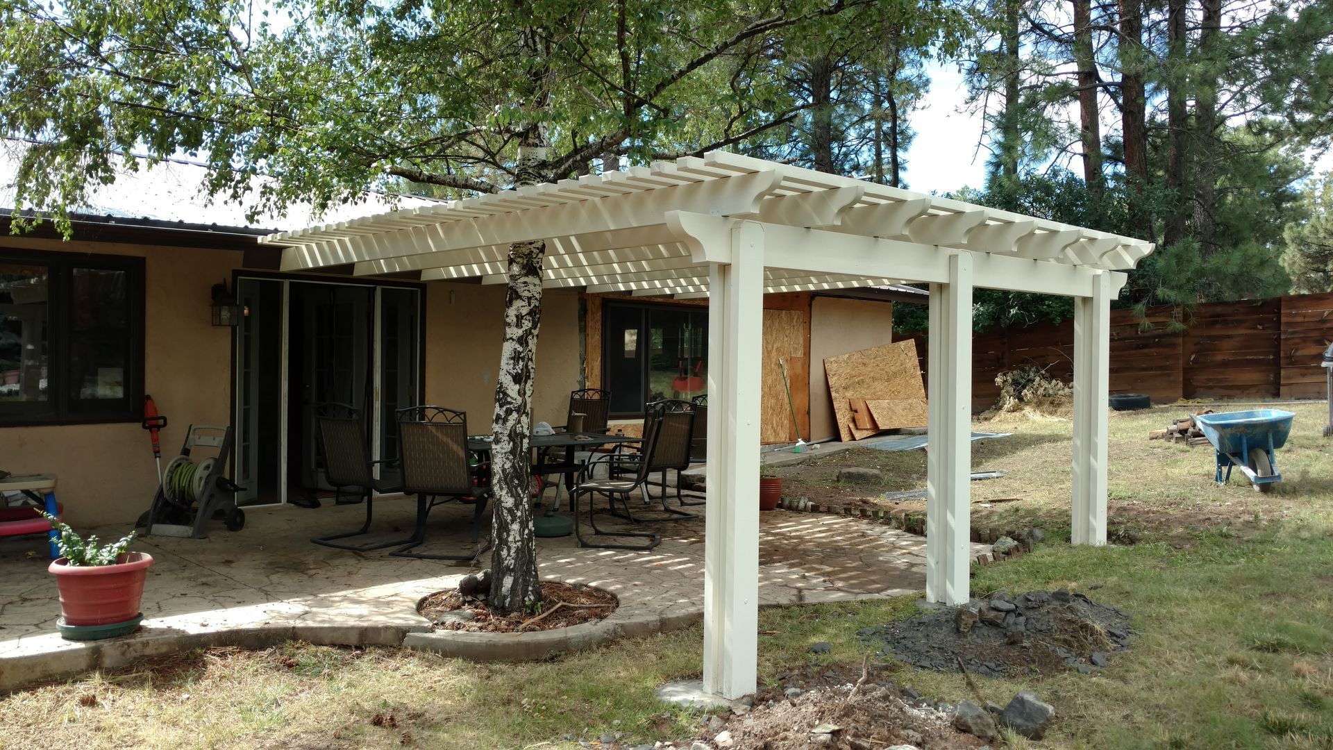 White pergola over a patio next to a house with outdoor furniture.