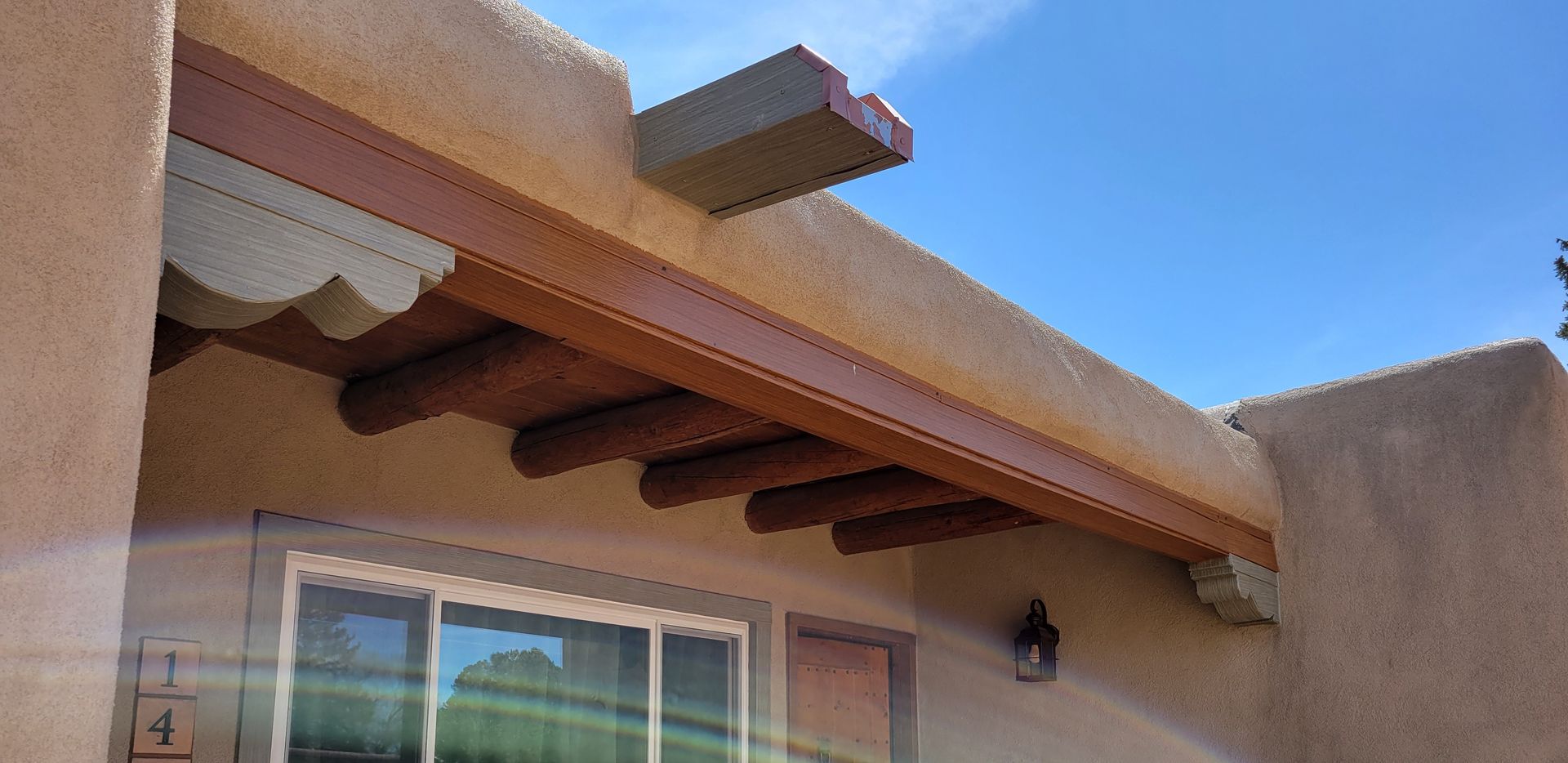 A southwestern-style building with a brown wooden beam and protruding roof supports. Blue sky in background.