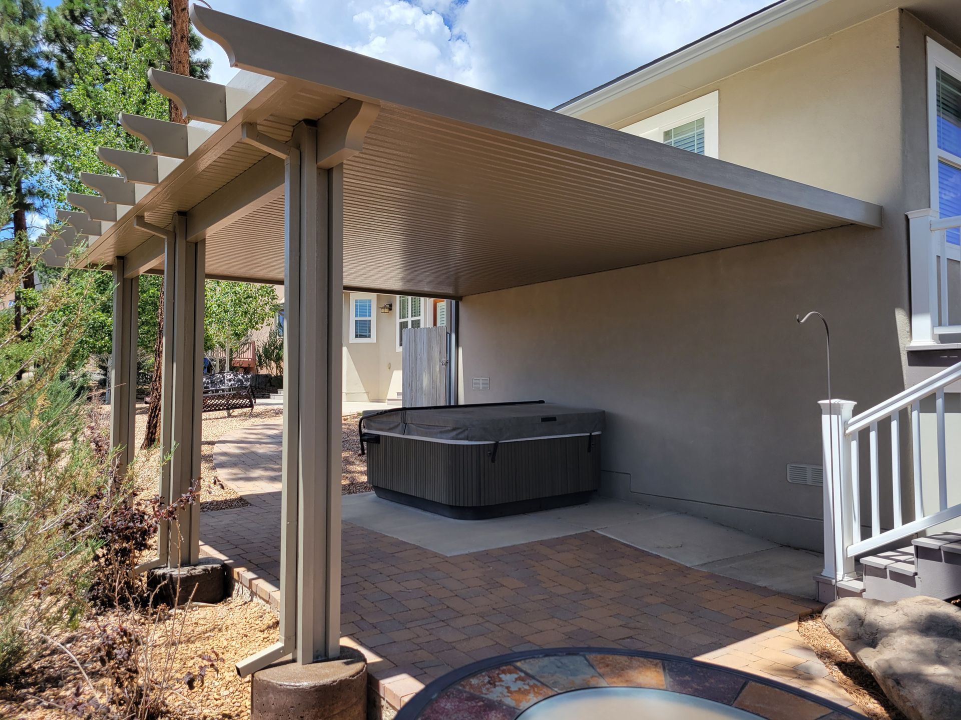 Outdoor patio with hot tub under a beige pergola attached to a light-colored house.