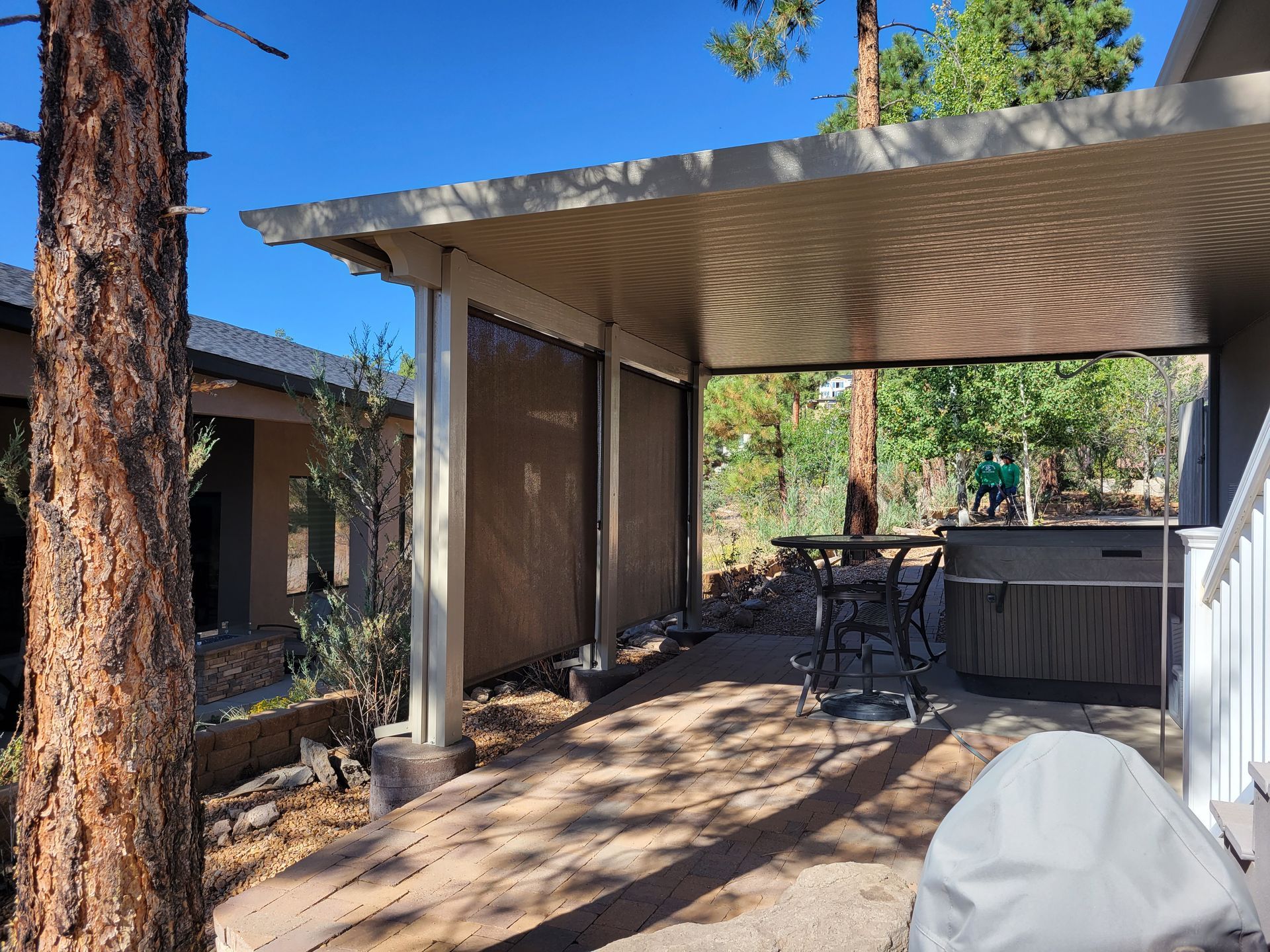 Covered patio with shade screens, hot tub, and trees in a sunny outdoor setting.