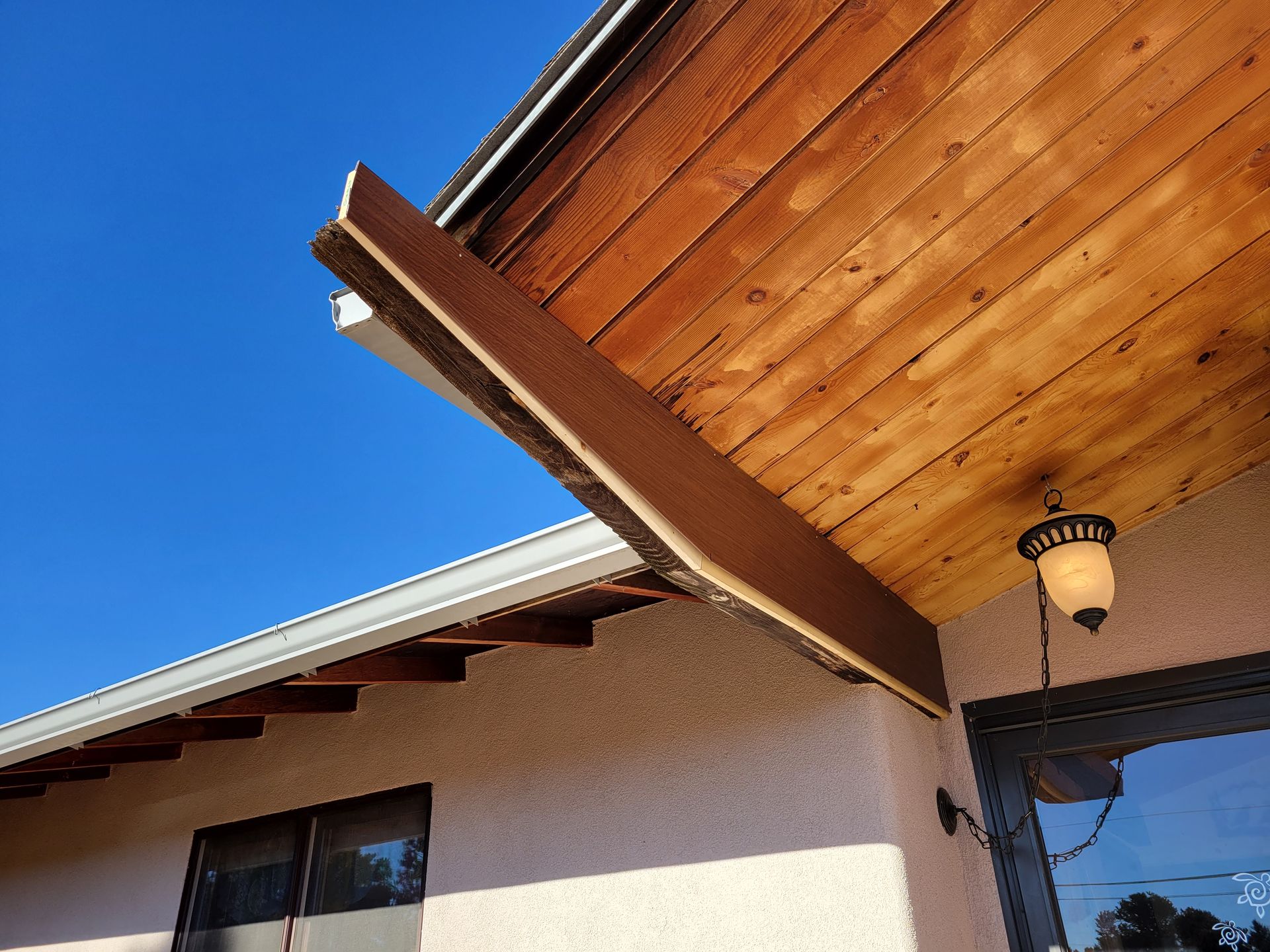 Exterior view of a building with a damaged wooden beam extending from the roof, beige stucco walls, and a blue sky.