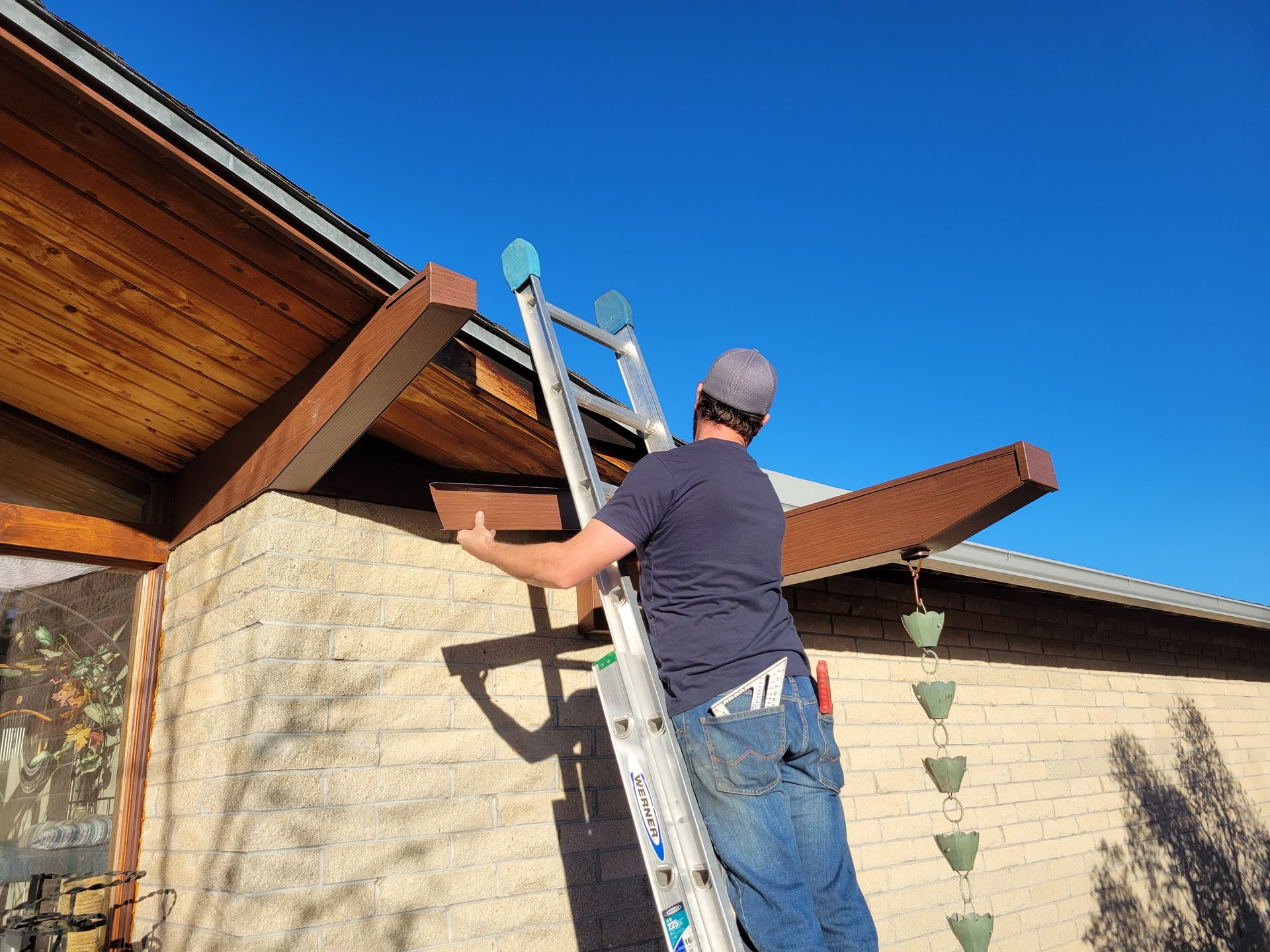 Person on ladder repairs soffit of a house; sunny day, blue sky.