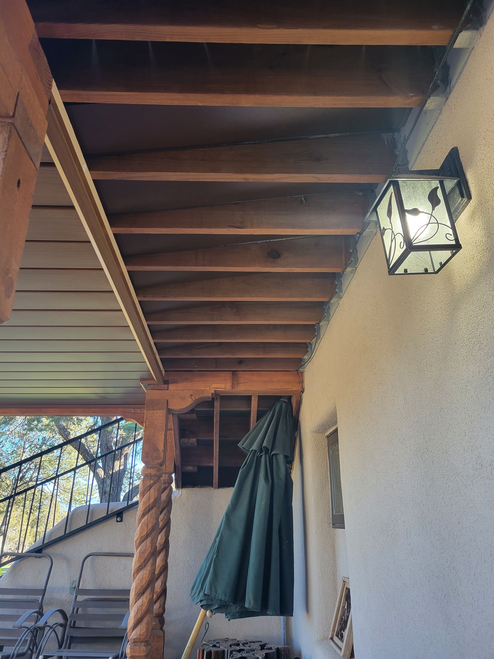 Wooden porch ceiling with exposed beams, an exterior light, and a green umbrella.