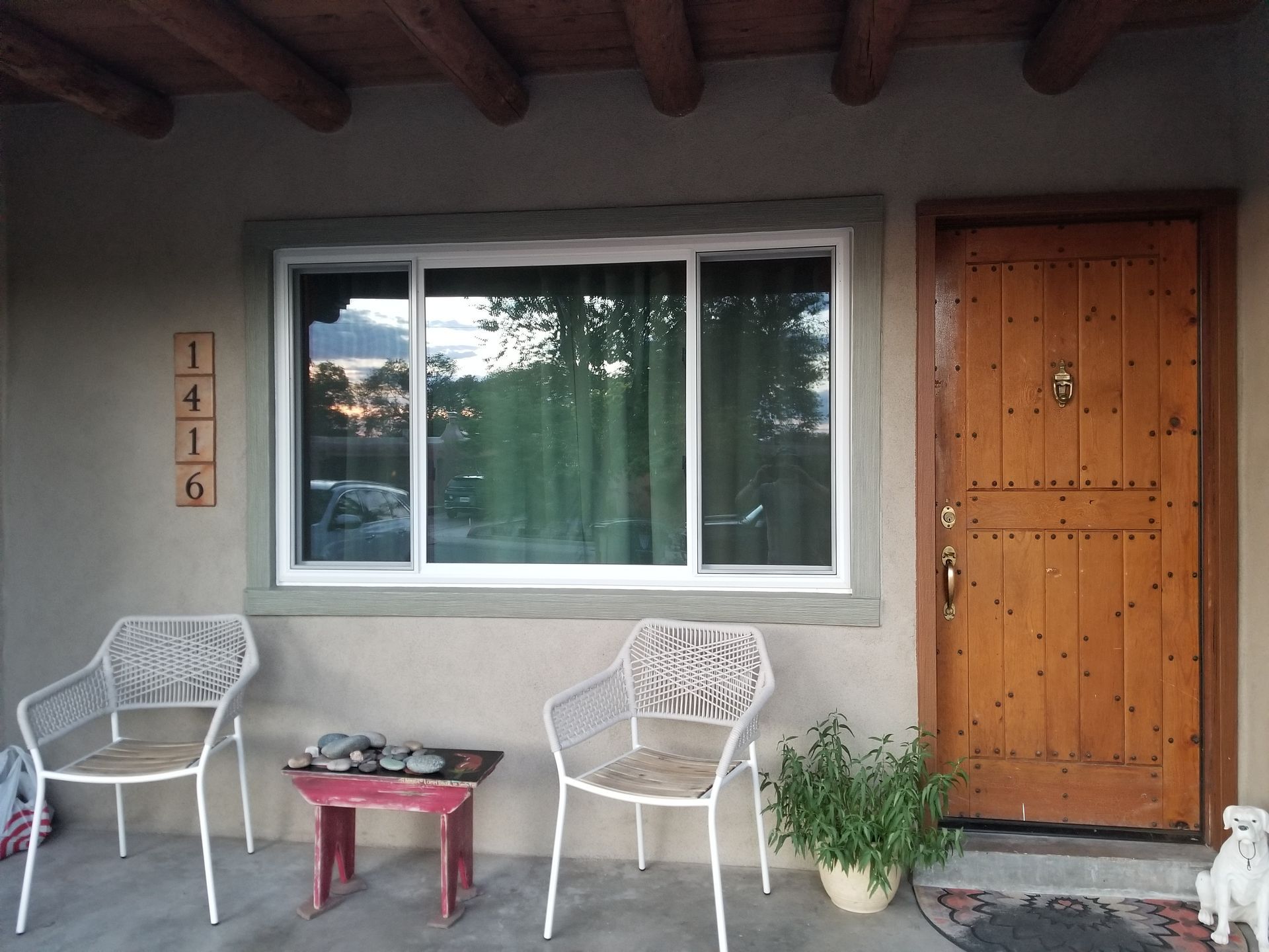 Front porch with two white chairs, a small table, window, and wooden door.