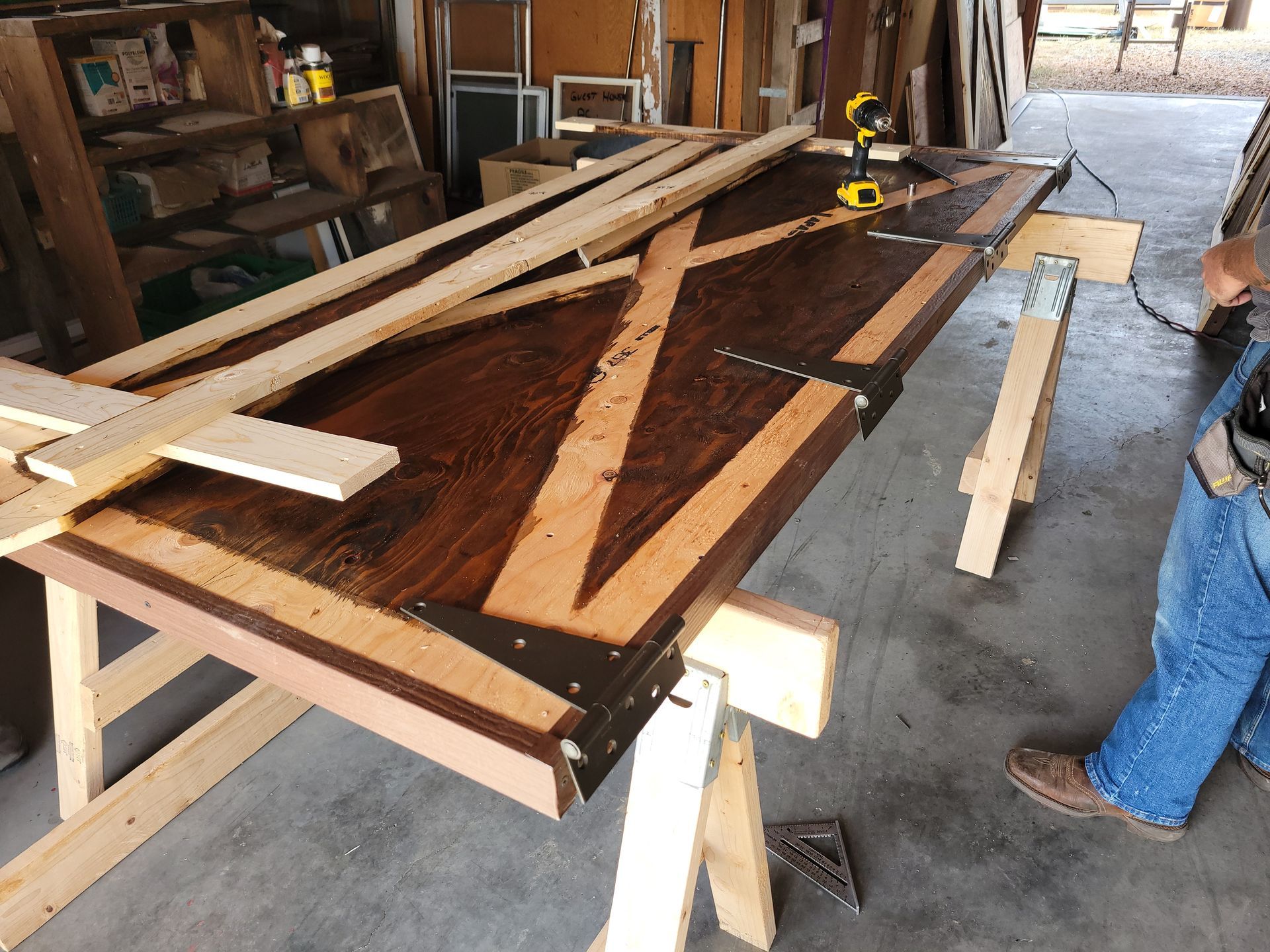 Person working on a wooden table, using a drill. Light wood pieces are laid on the stained, dark-brown surface.
