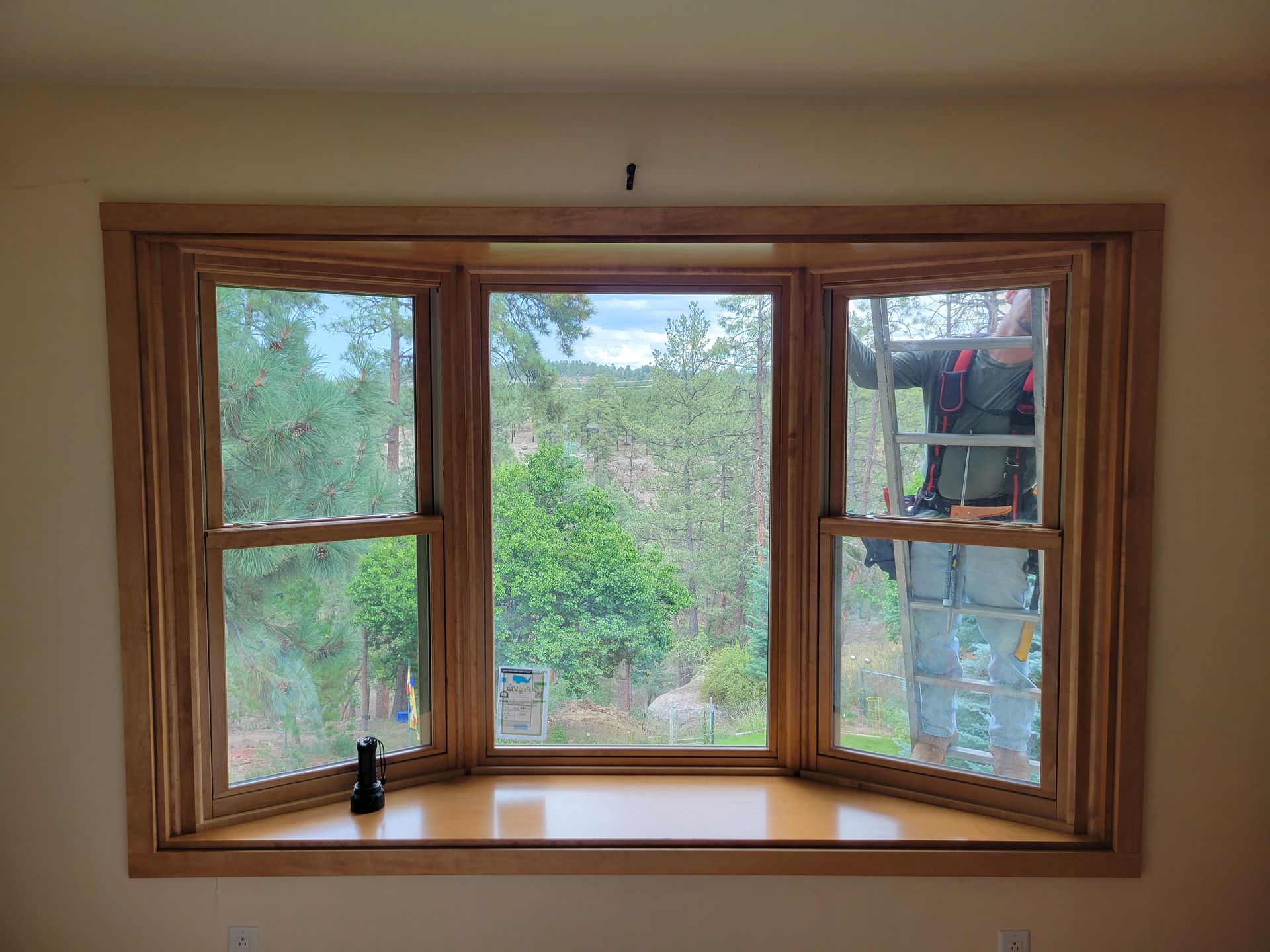 Bay window with wood trim, open side windows, person on a ladder cleaning the right window.